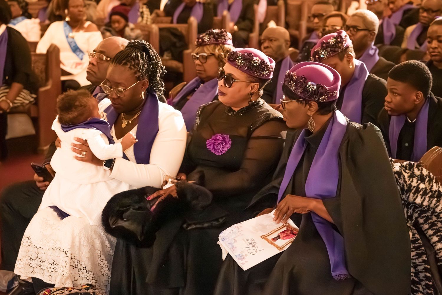 Guests in formal attire with purple accents seated in rows at an elegant ceremony.