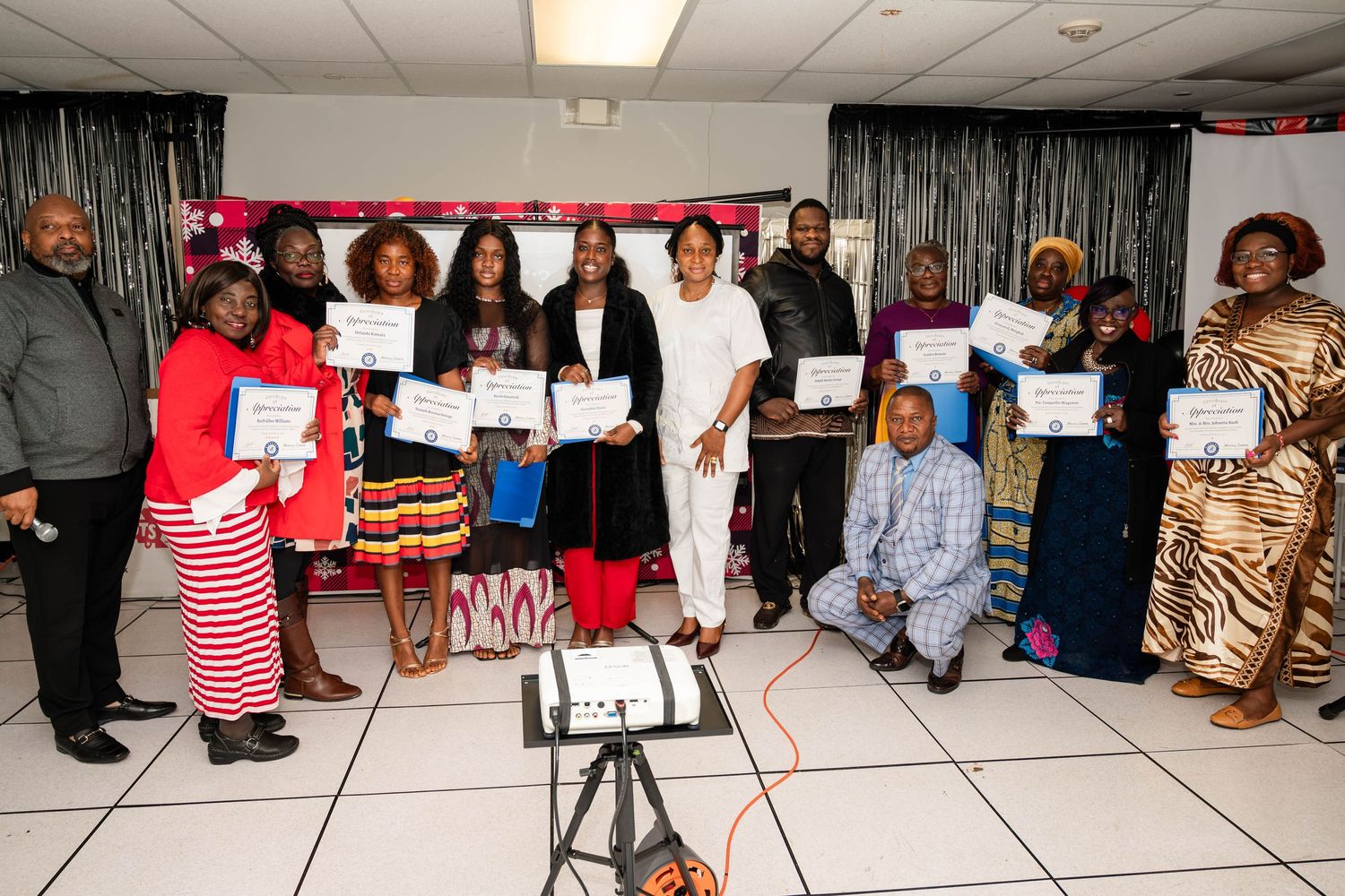 A group of people holding certificates pose together in a room with a silver backdrop for a celebration event.