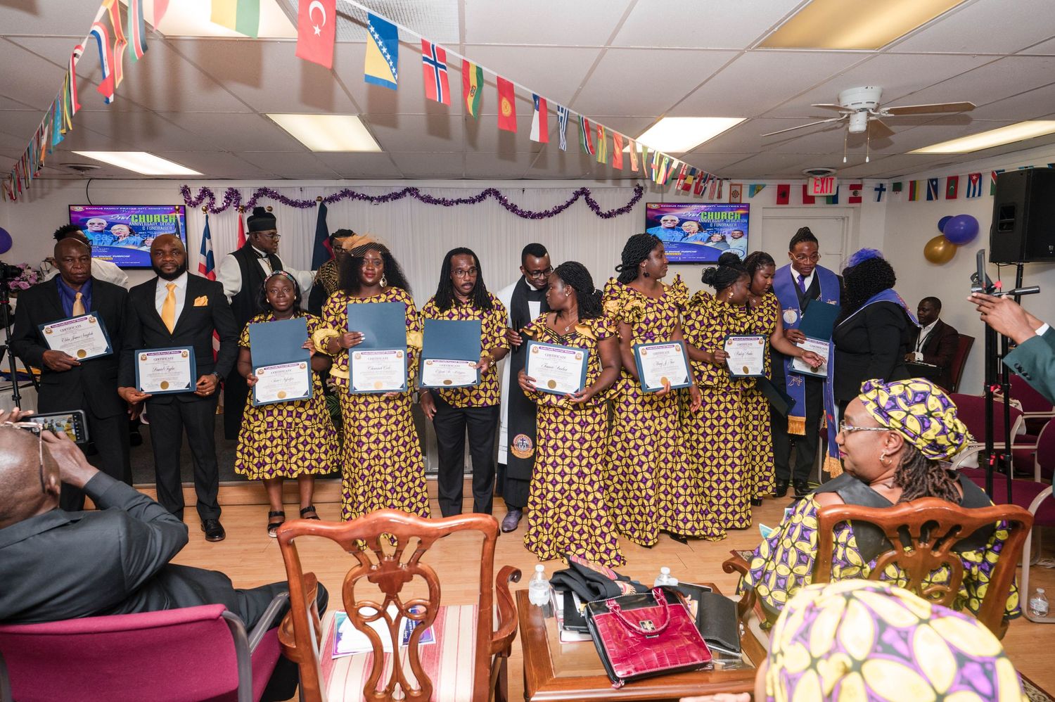Group of people in matching African print outfits gather in a room decorated with international flags.