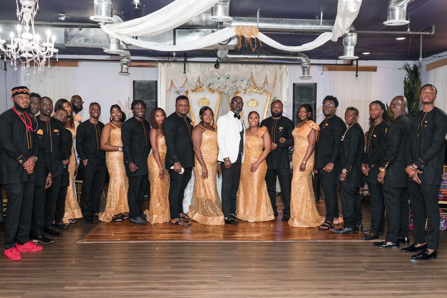 Wedding party poses showing bridesmaids in gold gowns and groomsmen in black suits at an indoor venue.