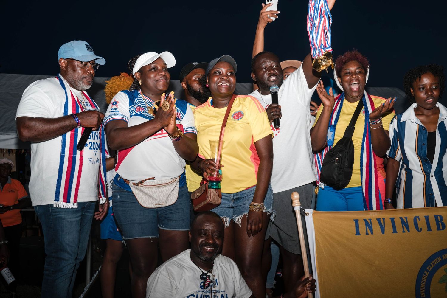 Group celebrates sports victory with trophies and medals against dark background.