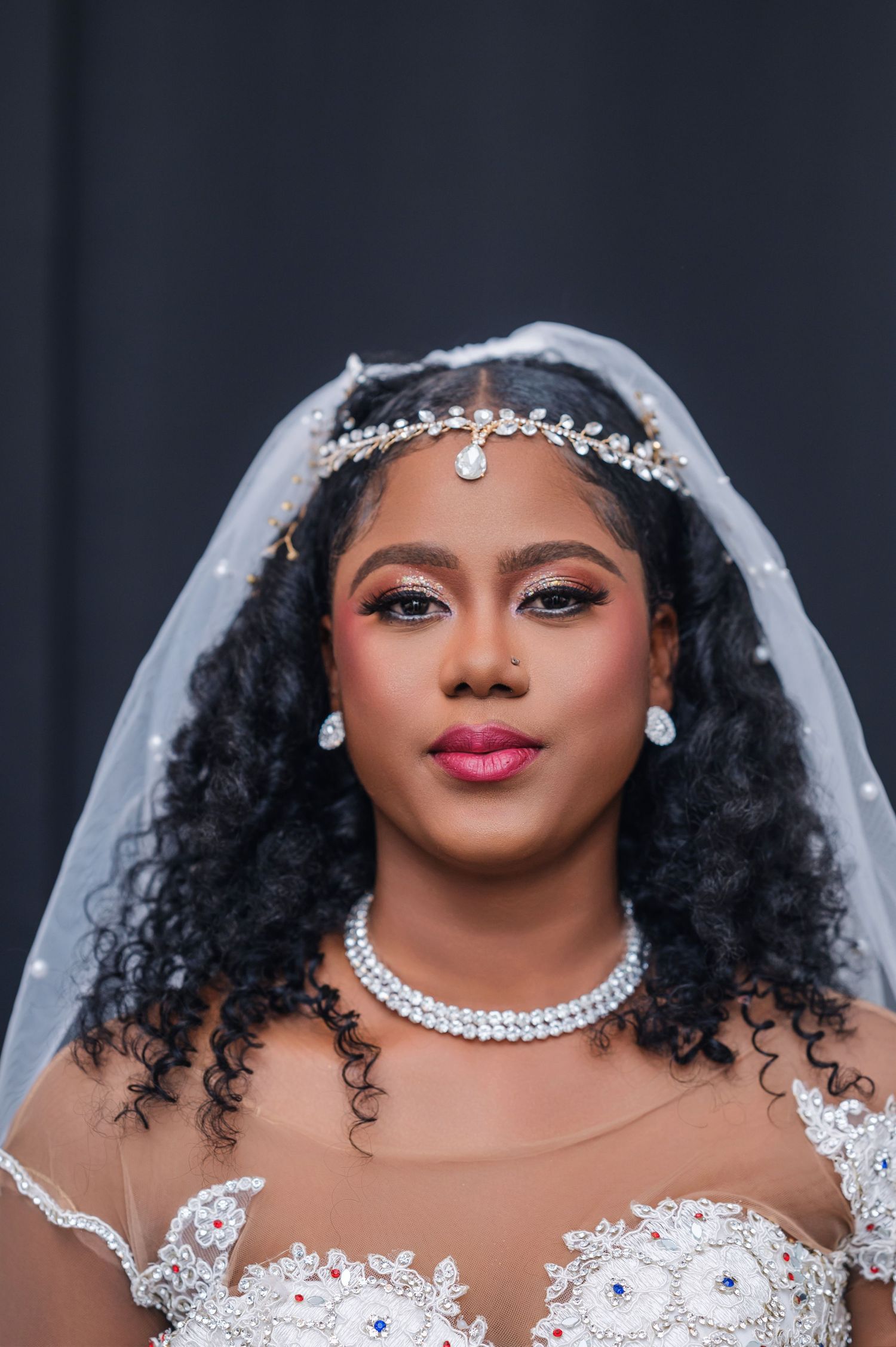Beautiful bride wearing pearl headpiece, necklace and sheer lace wedding dress with natural curly hair and glam makeup.