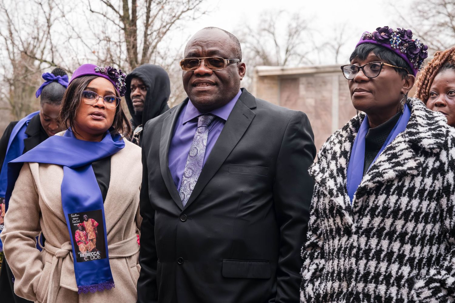 People in formal attire with purple accessories gather outside on a winter day.