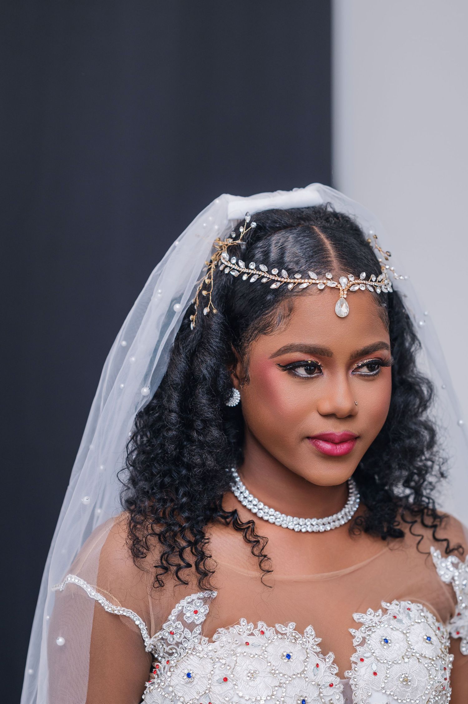 Beautiful bridal portrait featuring curly black hair, crystal headpiece, white lace gown, and elegant diamond necklace.