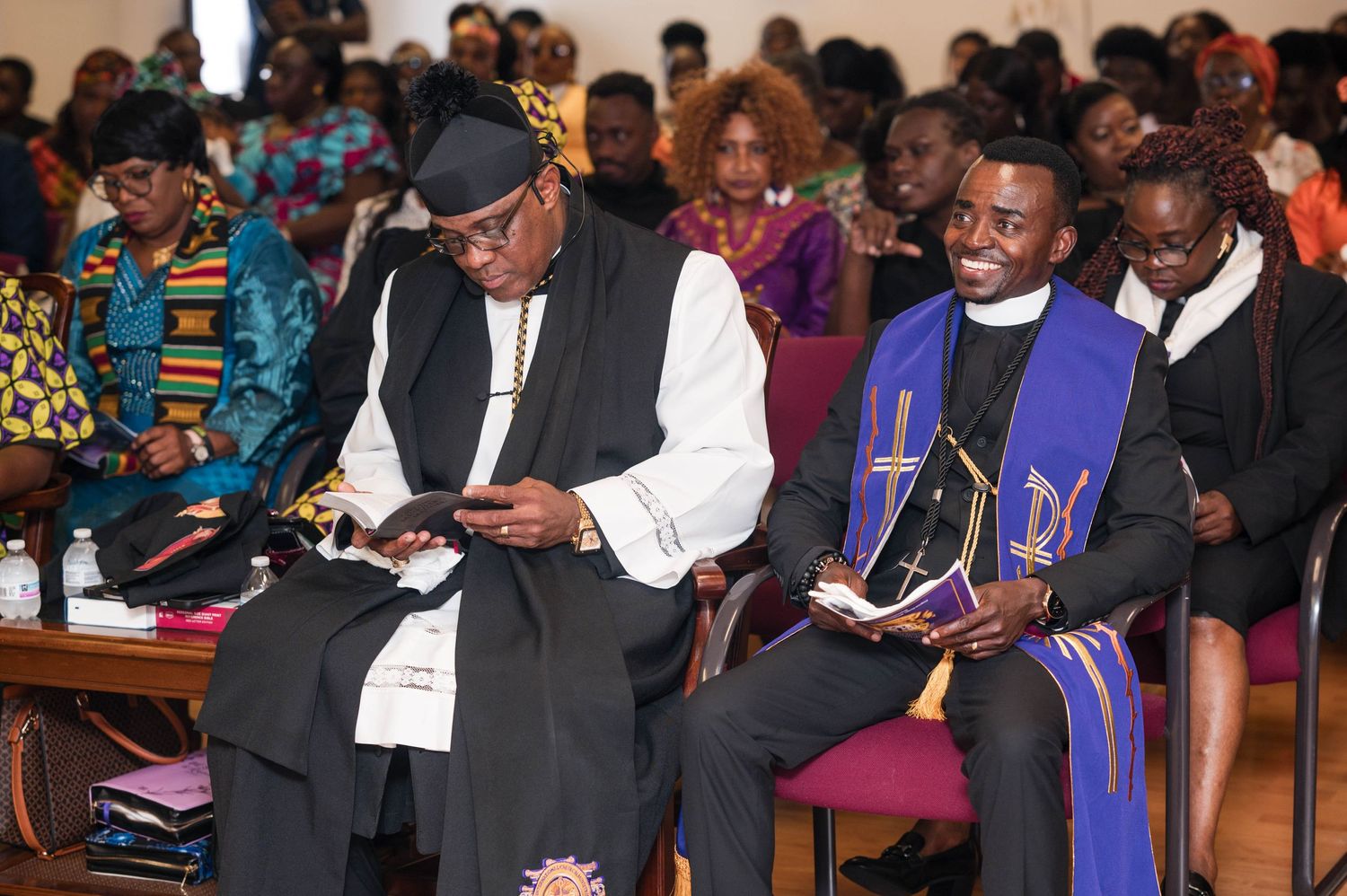 Attendees in traditional African and formal attire gather in a church or auditorium setting.