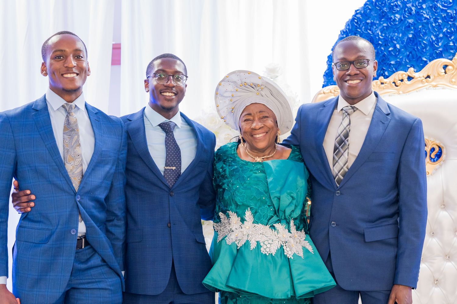 A group photo with three men in blue suits and a woman in a teal outfit with white lace details.