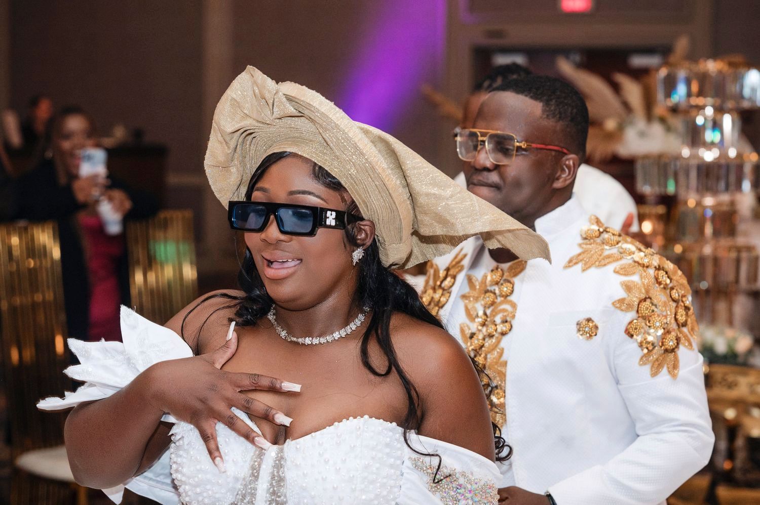 Two wedding guests wearing white attire and sunglasses dancing and enjoying themselves at a reception celebration.