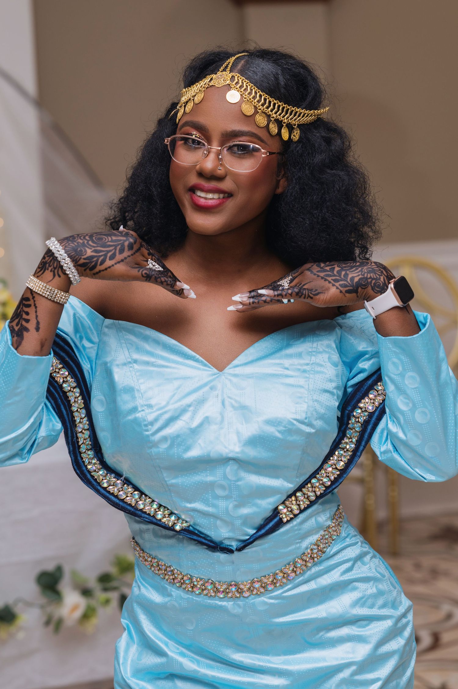 Person wearing a light blue formal dress with gold accents and a decorative gold headpiece in an elegant pose.