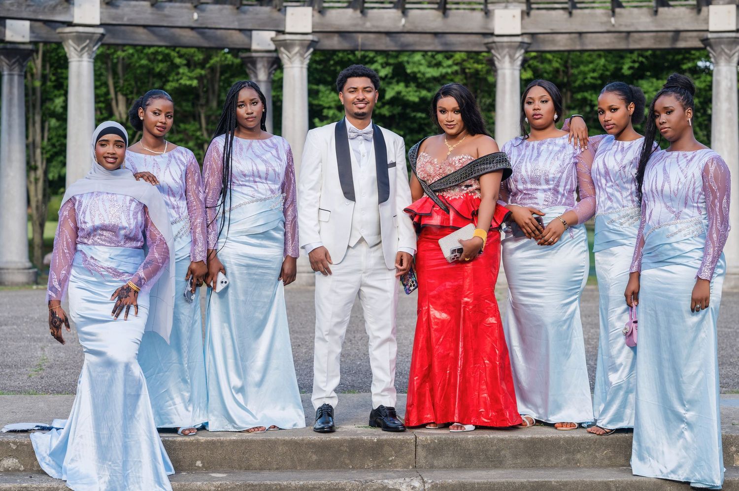 Wedding party poses in coordinated formal attire with bridesmaids in light blue gowns and couple in white and red.