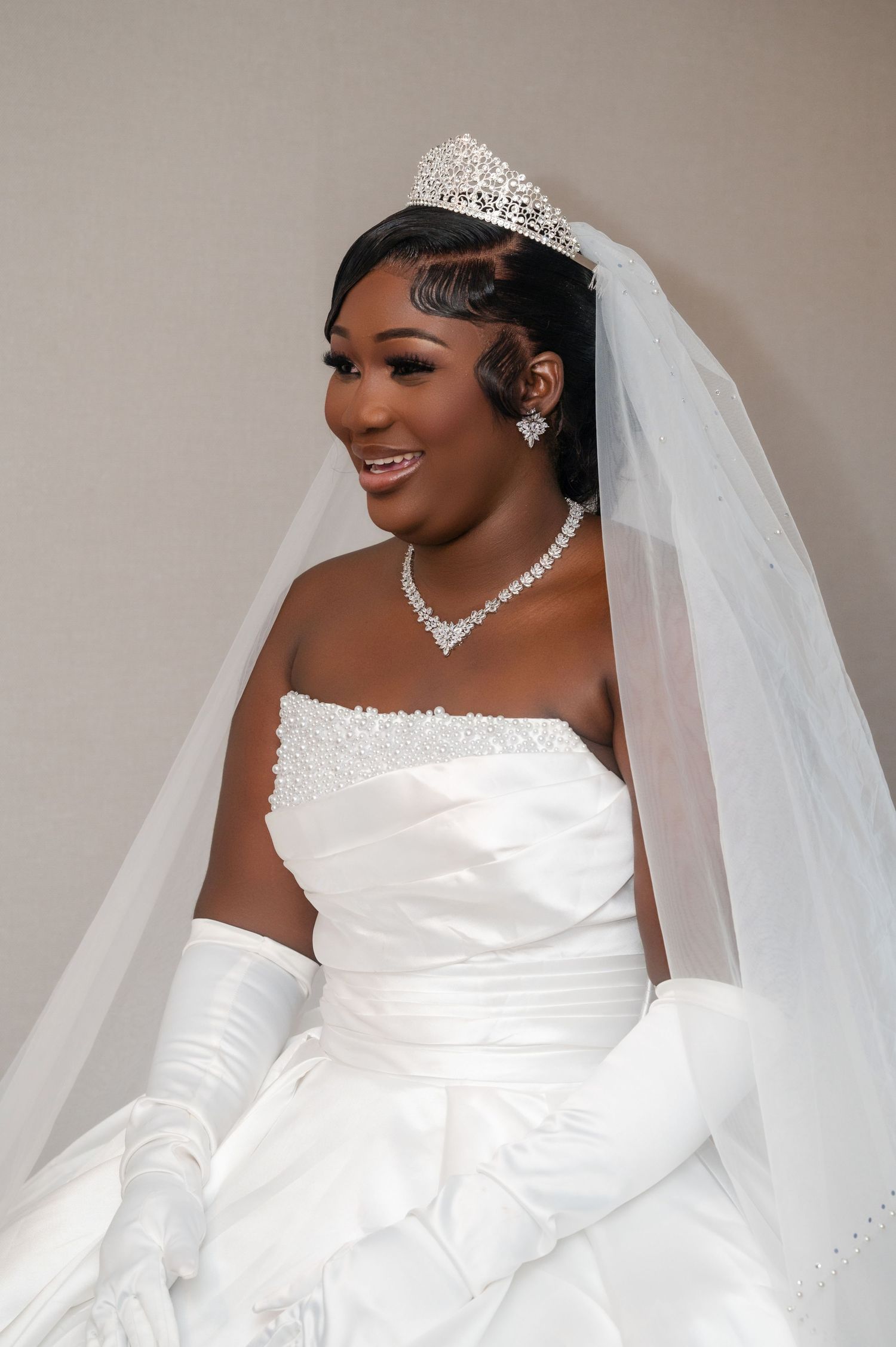 A radiant bride wearing a classic white strapless gown with long gloves, tiara and flowing veil on her wedding day.