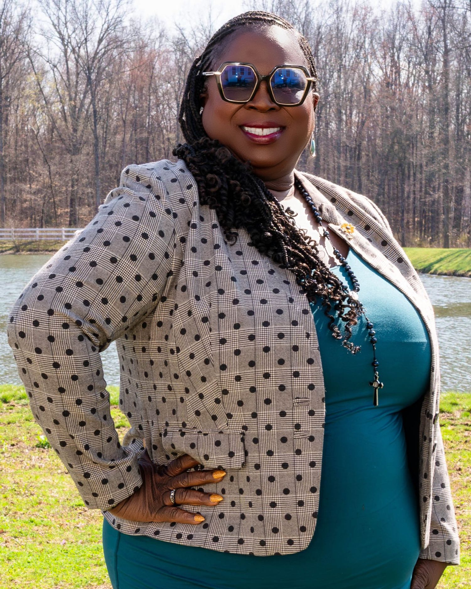 A polka dot blazer and teal dress create a stylish look for an outdoor photo by a lake on a fall day.