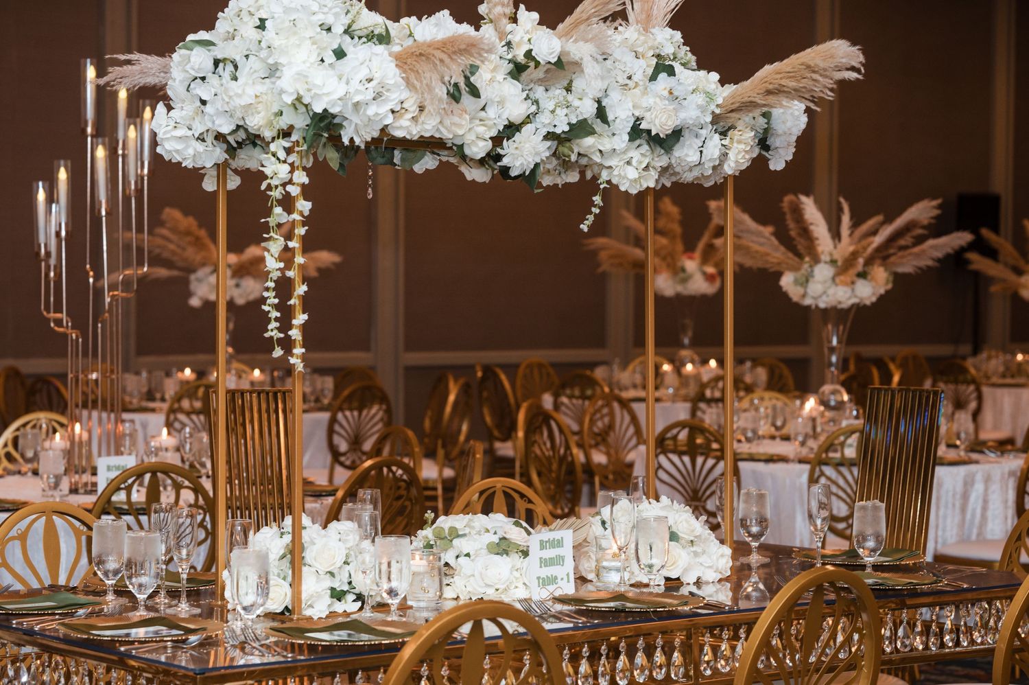 Elegant wedding reception table with tall gold centerpieces and white floral arrangements in a luxurious ballroom setting.