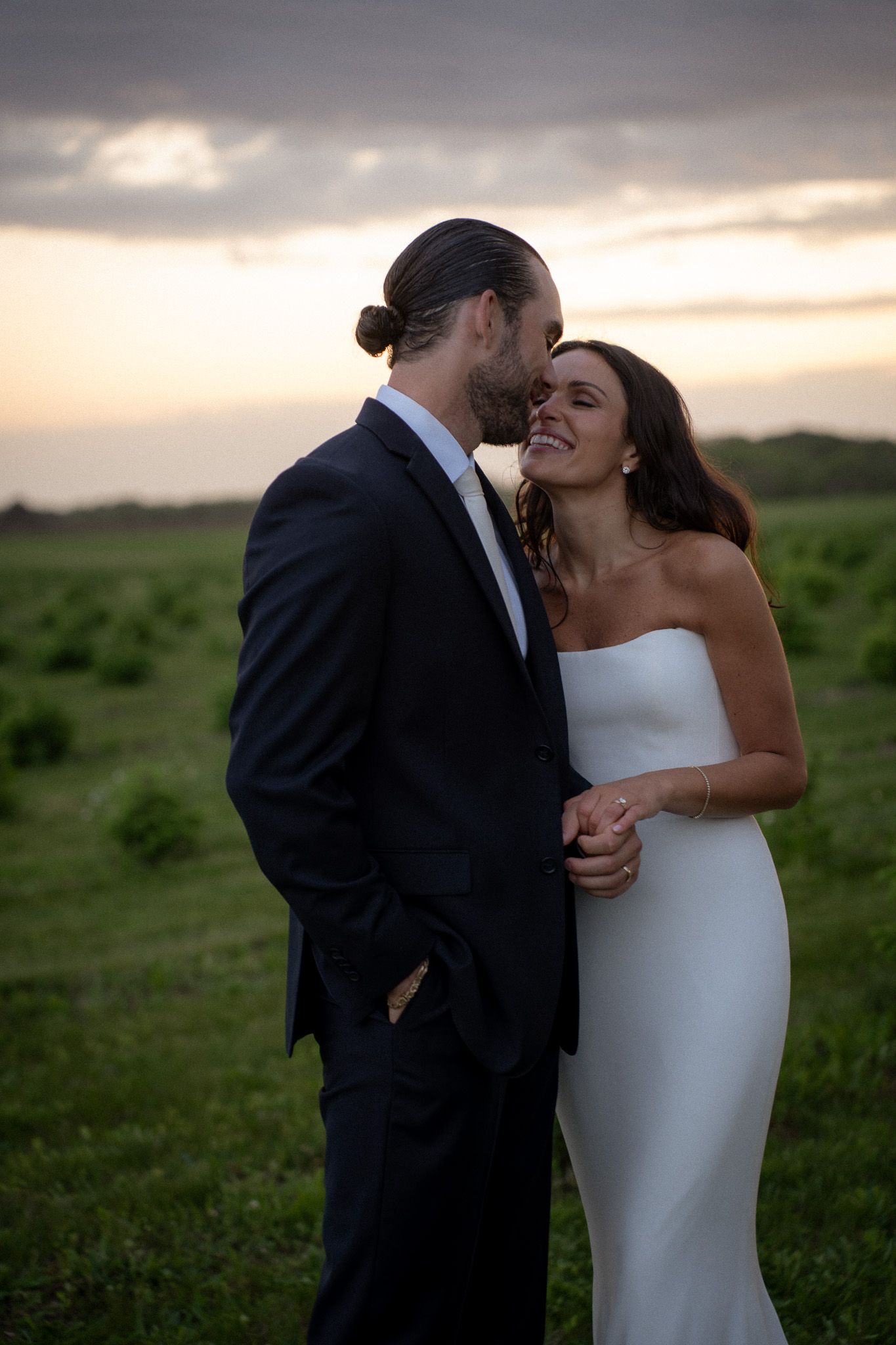 Couple embracing at sunset in an open field on Long Island, the bride in a strapless gown and the groom in a dark suit in Hamptons, NY