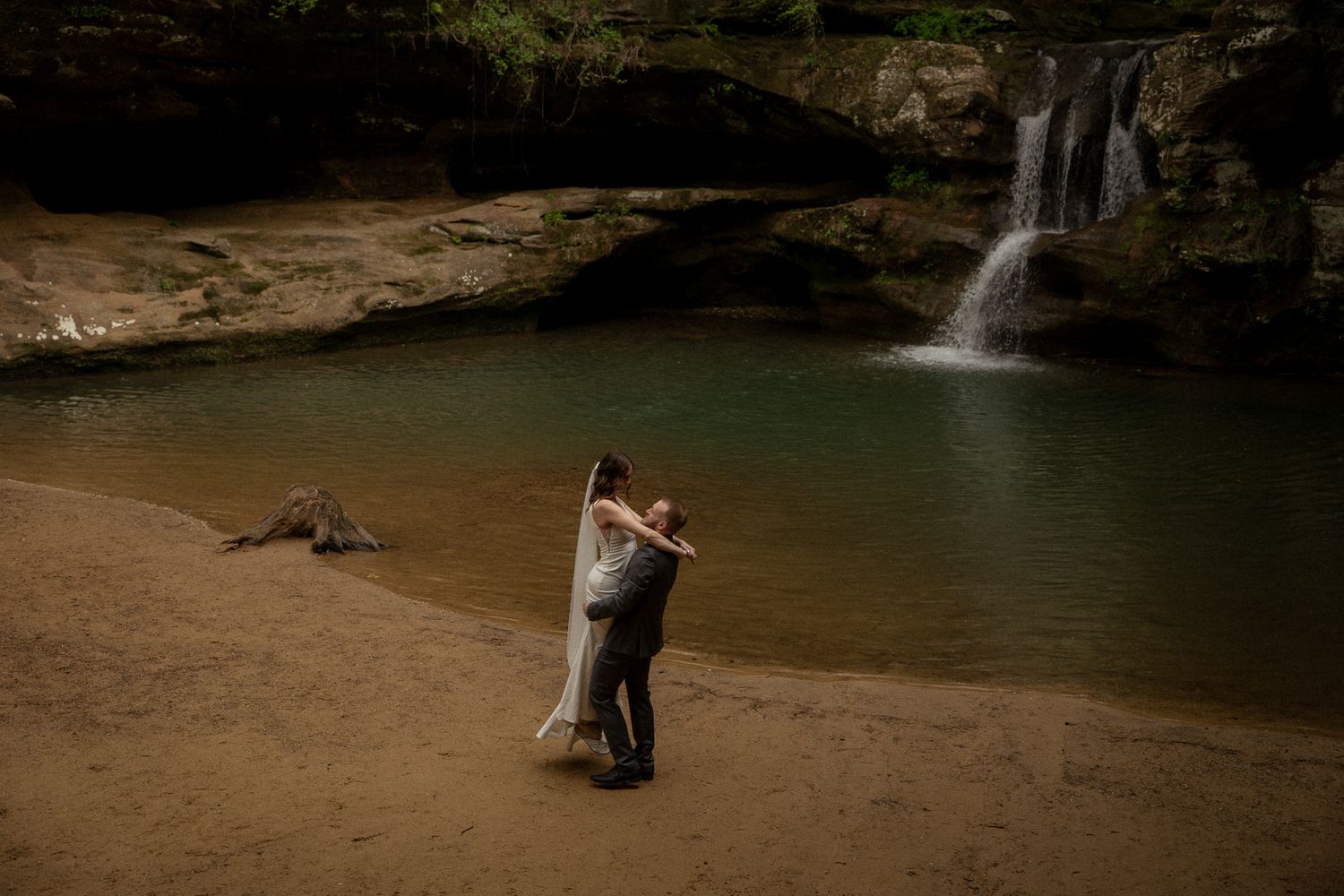 Bride and groom sharing a kiss on the sandy shore of a waterfall during their destination national park elopement.