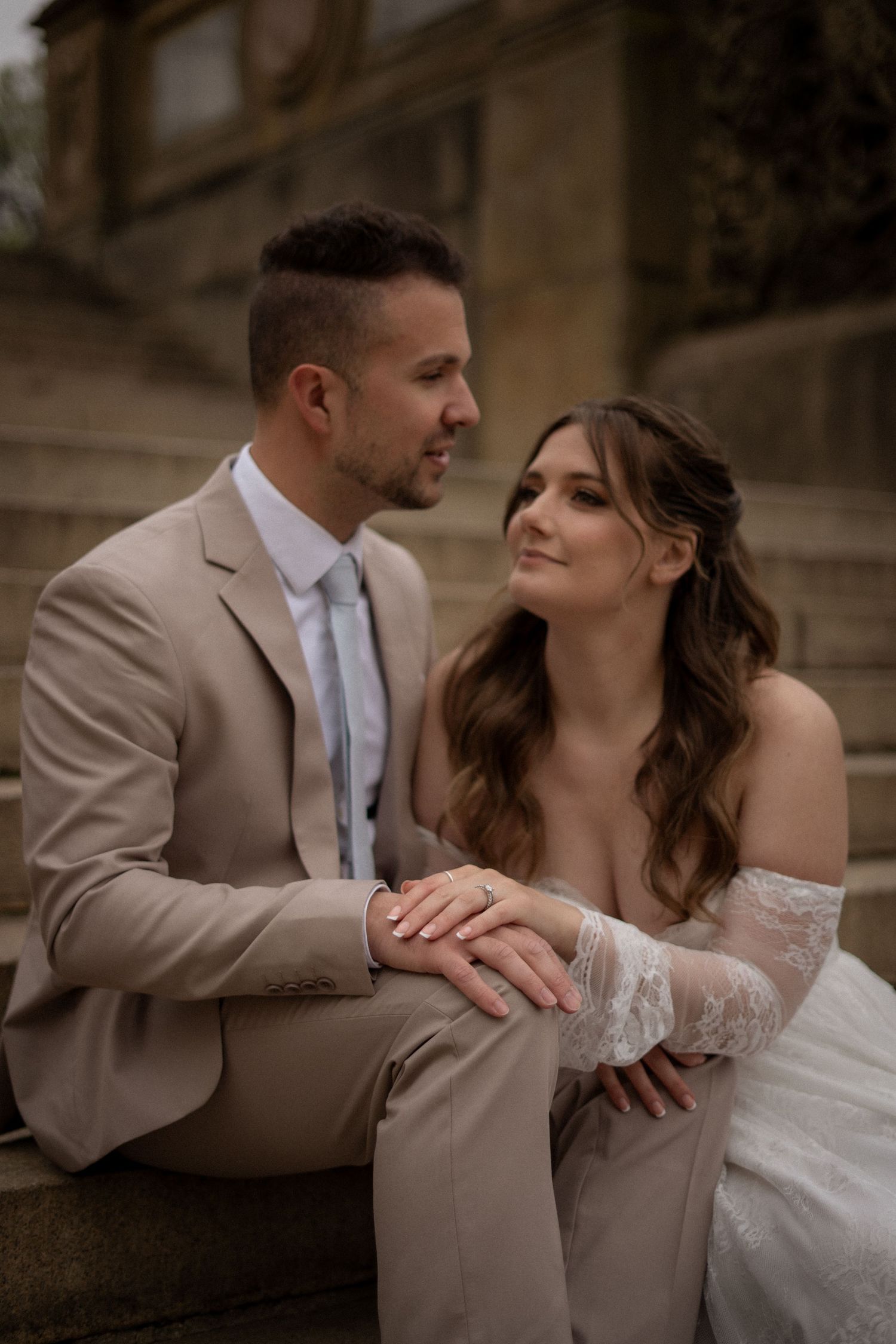 Bride and groom sitting on stone steps, holding hands and sharing an intimate moment at Bethesda Terrace, Central Park.