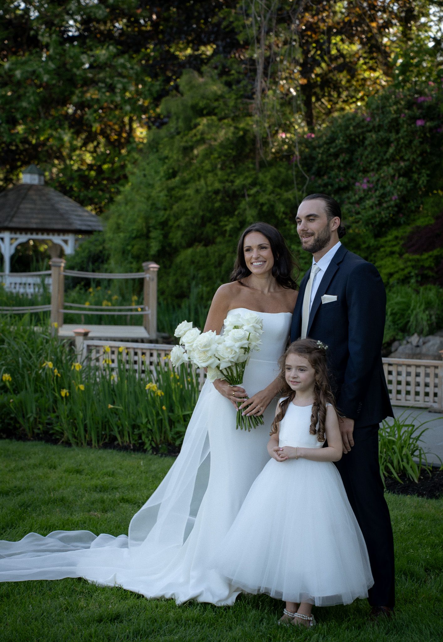 Bride, groom, and flower girl sharing a joyful moment in a garden setting in Hamptons, New York