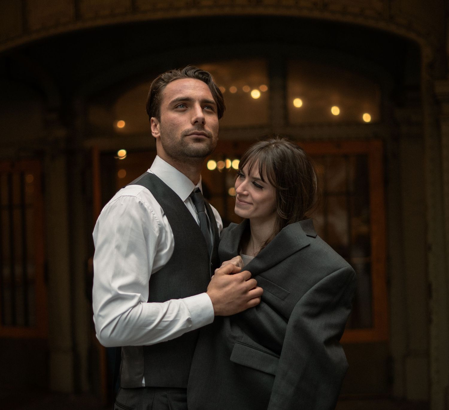 A couple in formal wear embrace under atmospheric lighting and arches.