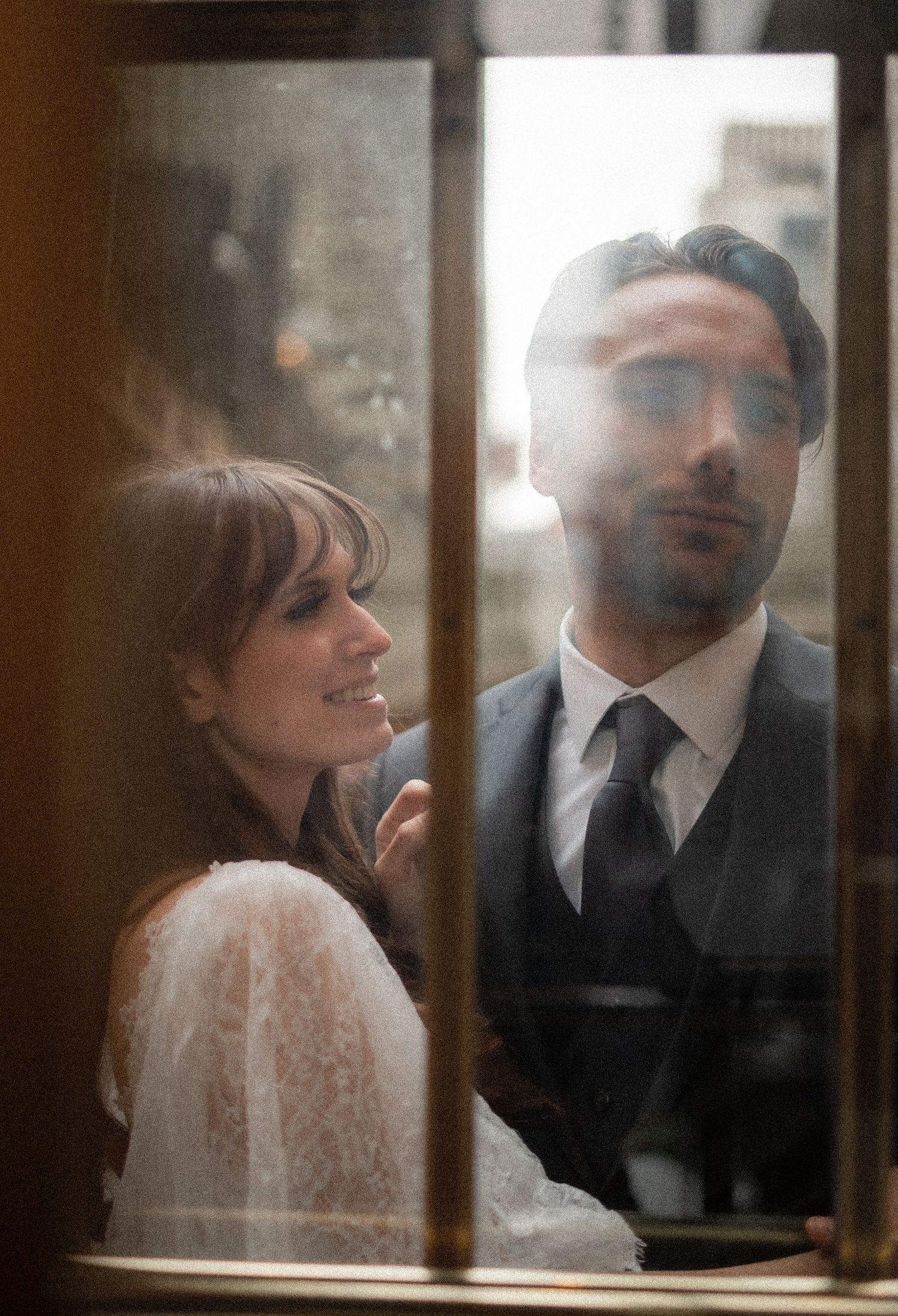 A dreamy window reflection of a couple in wedding attire sharing an intimate moment.
