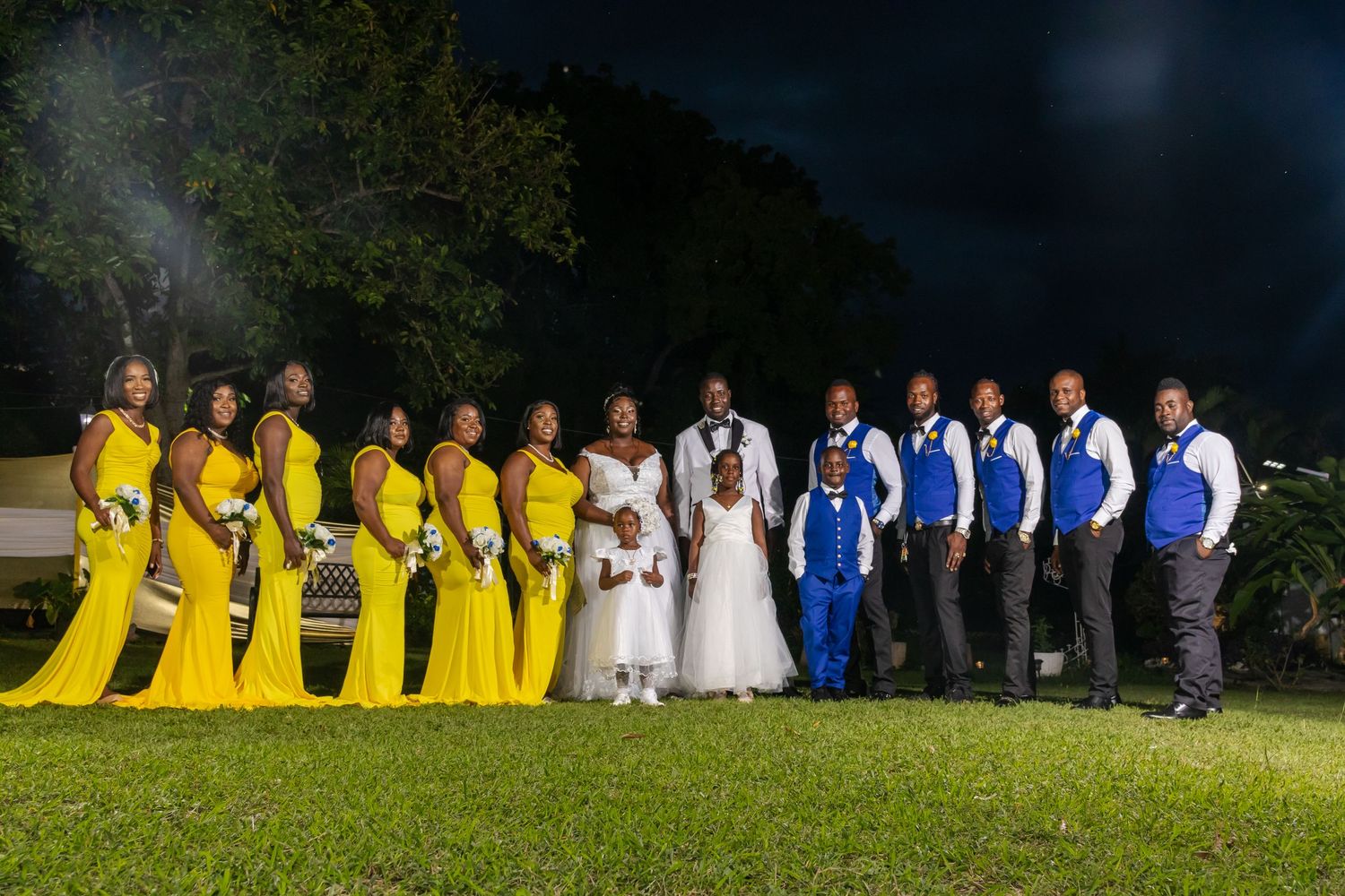 Wide angle photograph of bride and groom and bridal party after the wedding ceremony, where they are wearing yellow dresses and  blue suits