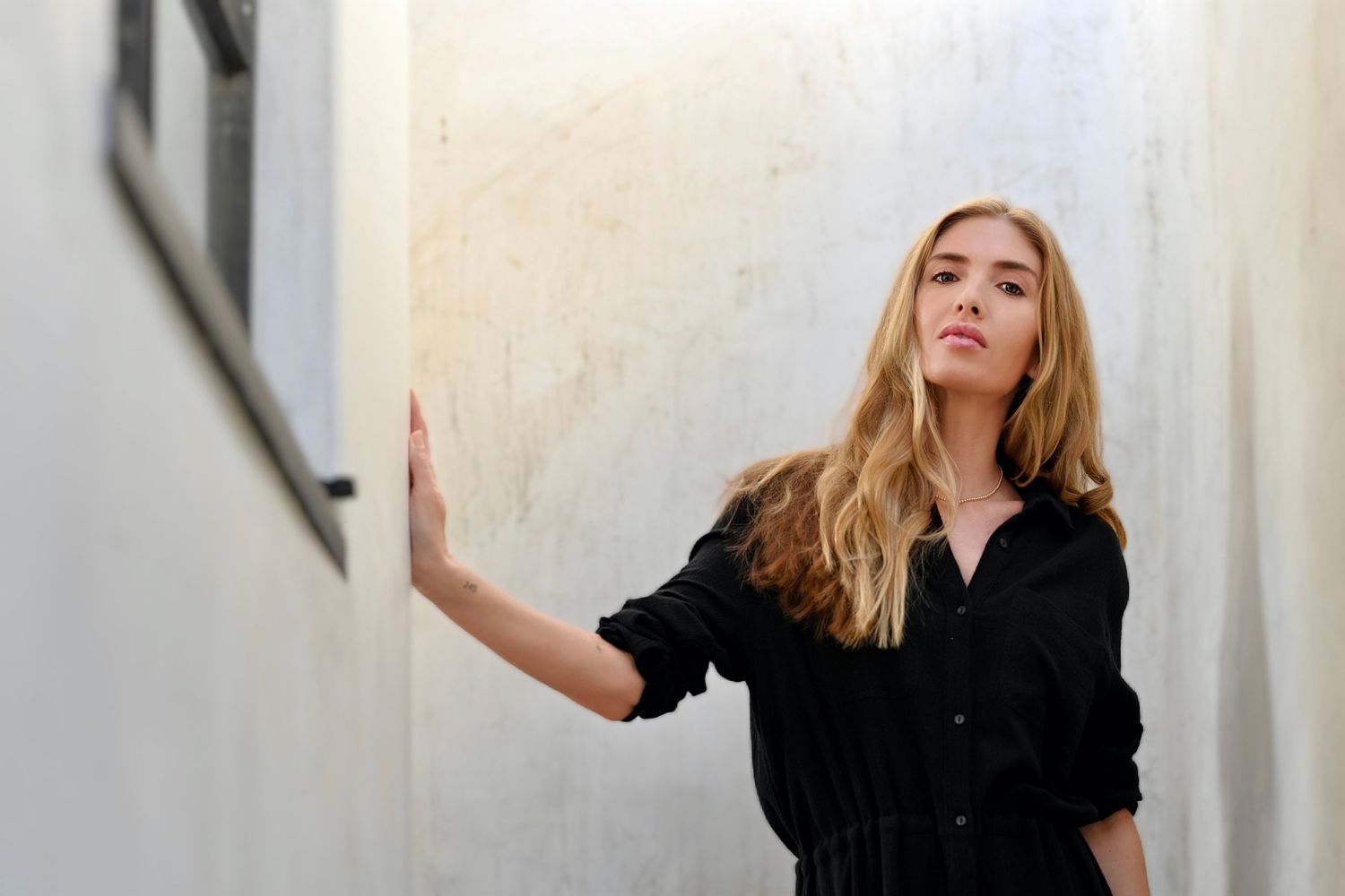 Woman in black dress poses against white wall in a series of dynamic fashion portraits.