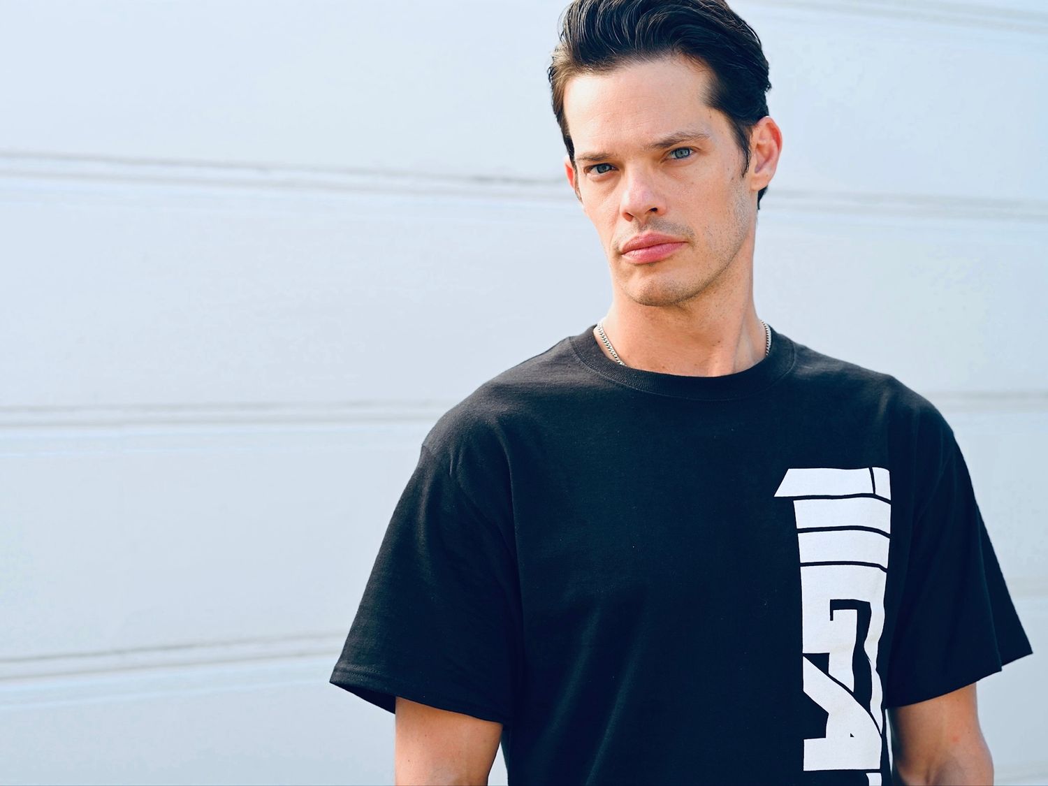 Portrait of person in black t-shirt with white vertical logo against light background.