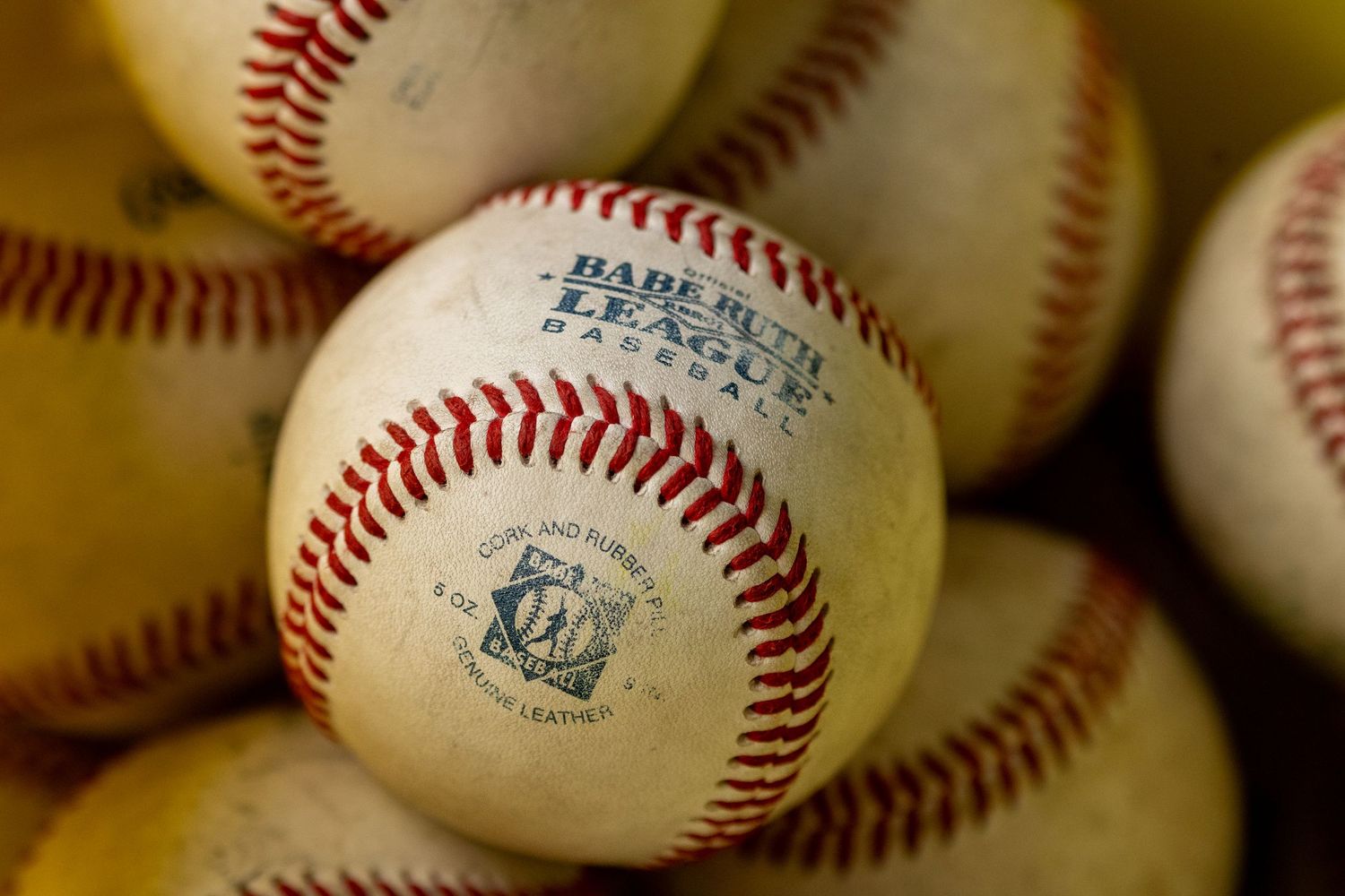 Close-up of Babe Ruth League baseballs with red stitching stacked together.