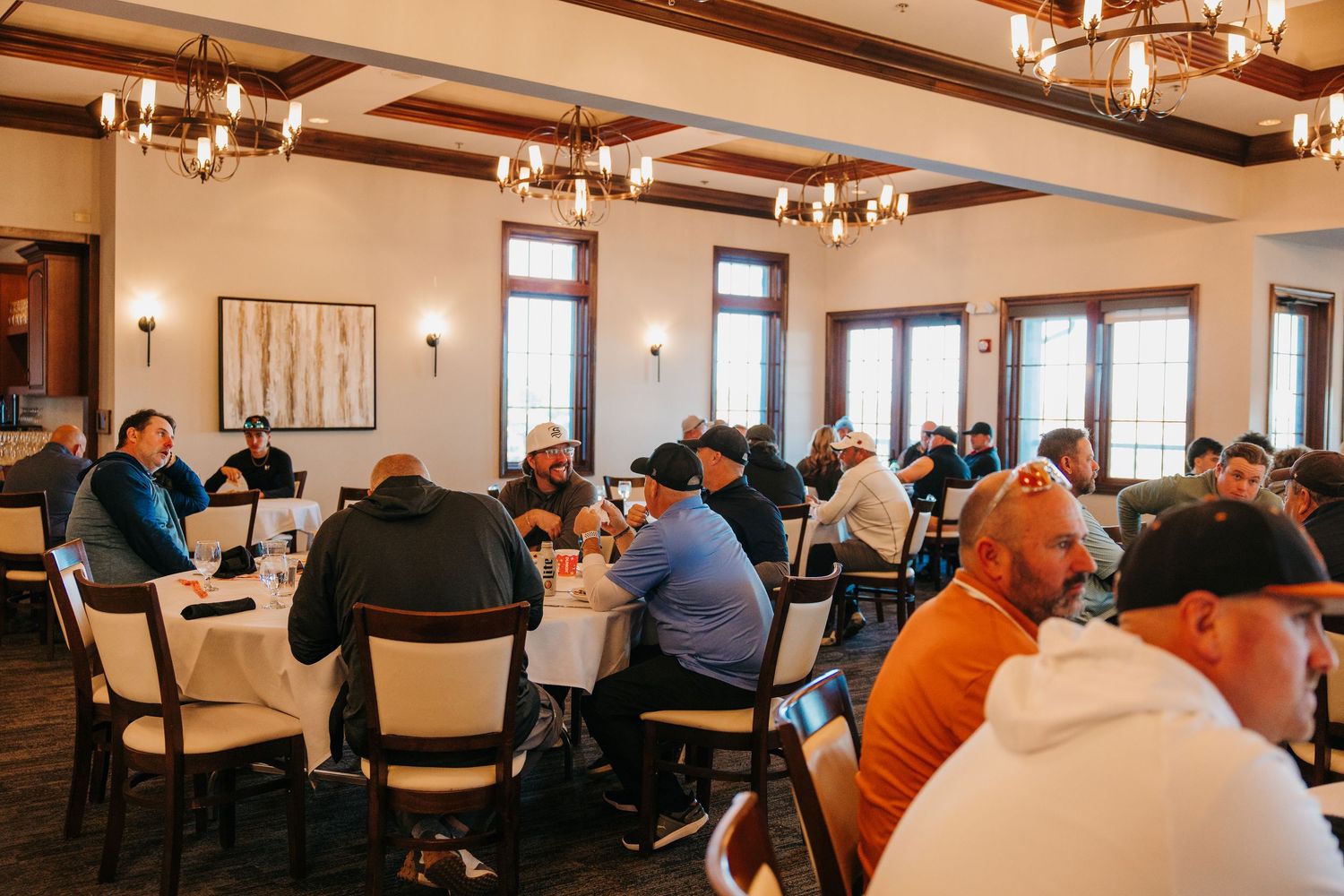 Golfers enjoy a post-tournament lunch in an elegant clubhouse dining room with chandeliers.
