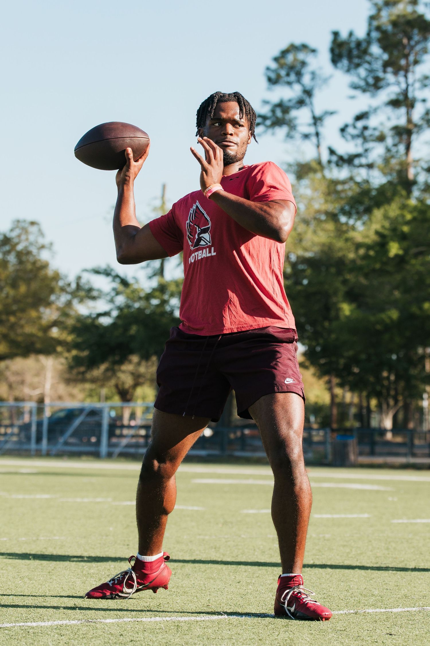 Young football player in red Cardinals shirt prepares to throw a football on a green field.