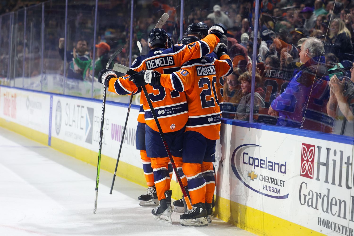 Hockey players in orange uniforms celebrate a goal against the boards during an AHL game.