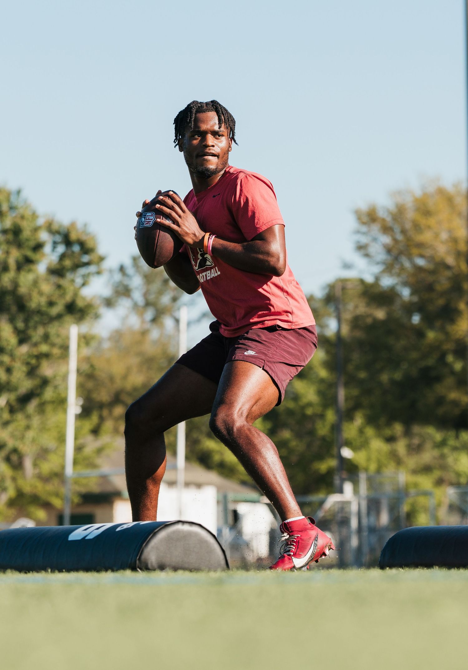 A football player in a red uniform practices throwing drills on a green field during an outdoor training session.