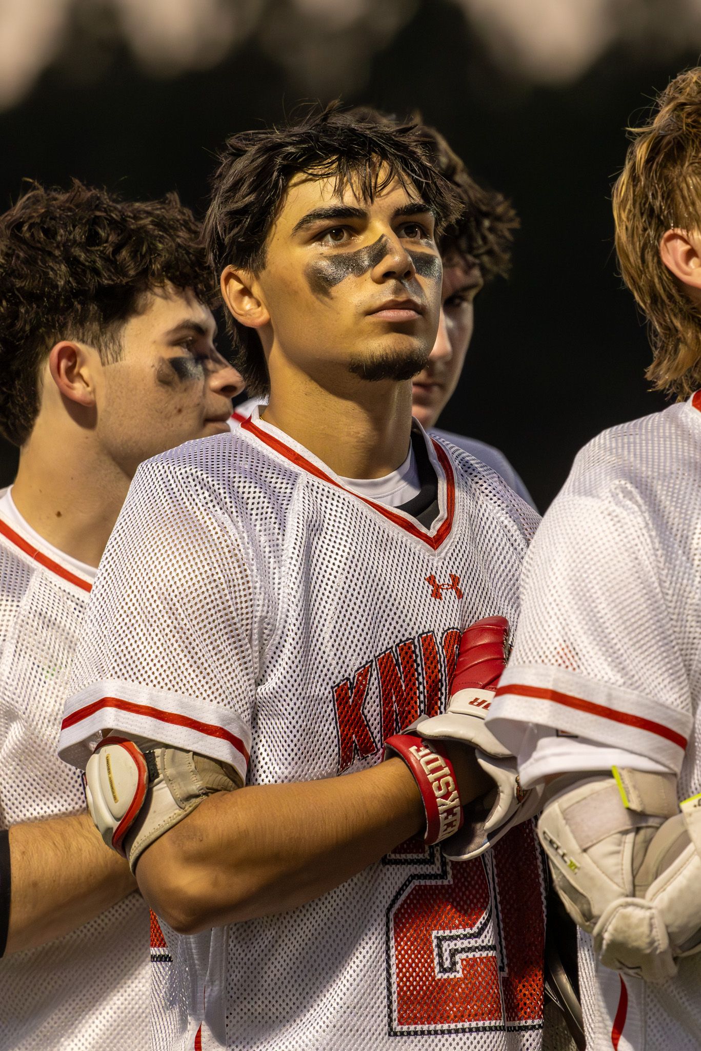 Young lacrosse players in white Knights uniforms with eye black, standing together during a pregame ceremony.