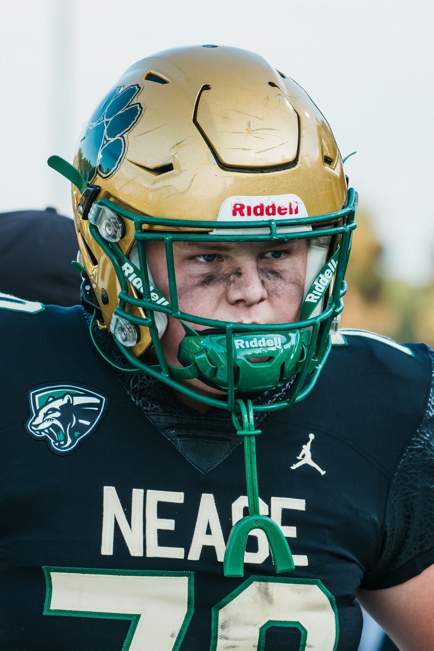 Football player wearing a gold Riddell helmet and black NEACE jersey with number 78 on the field.