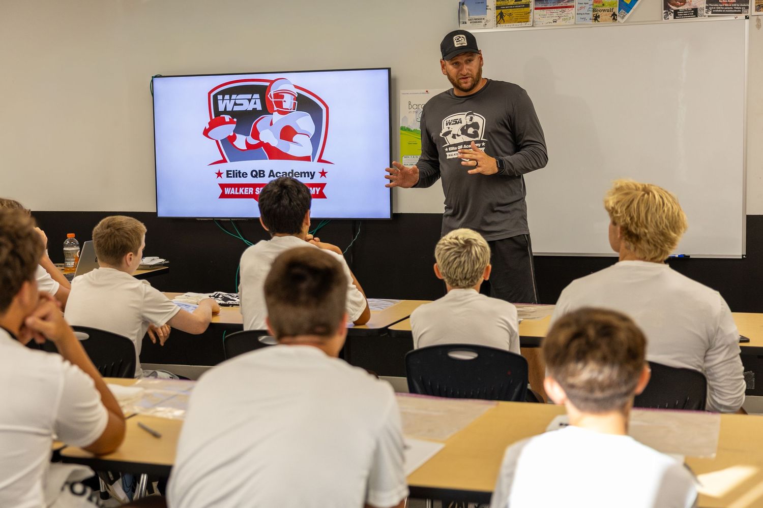 Football coach presents QB Academy slides to young students in a modern classroom setting.