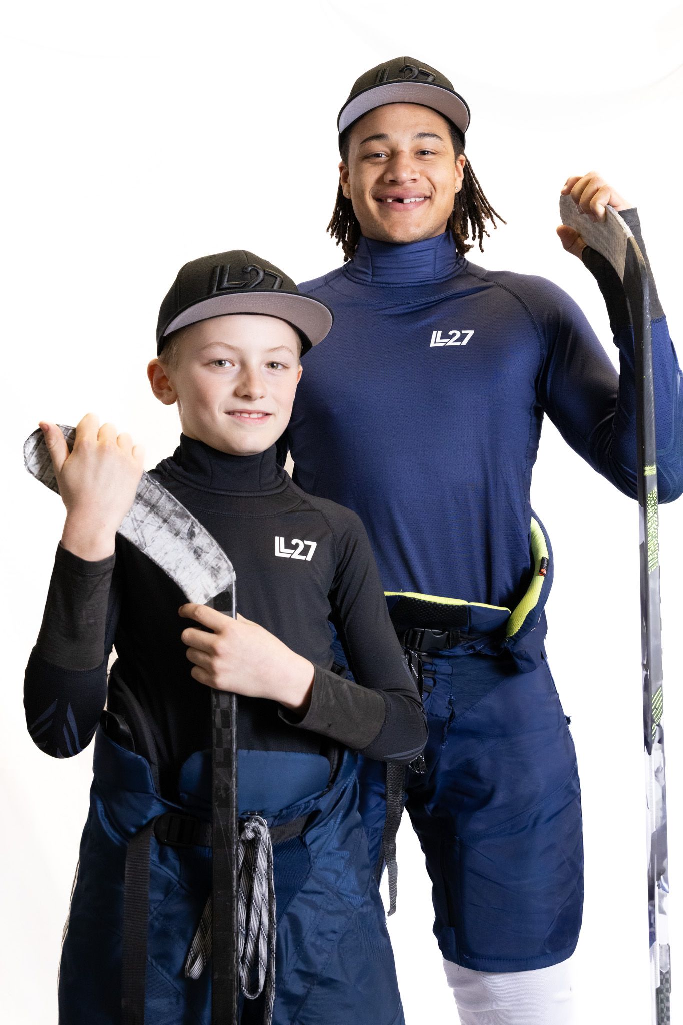 Two youth hockey players in IL27 gear pose with sticks against a white background.