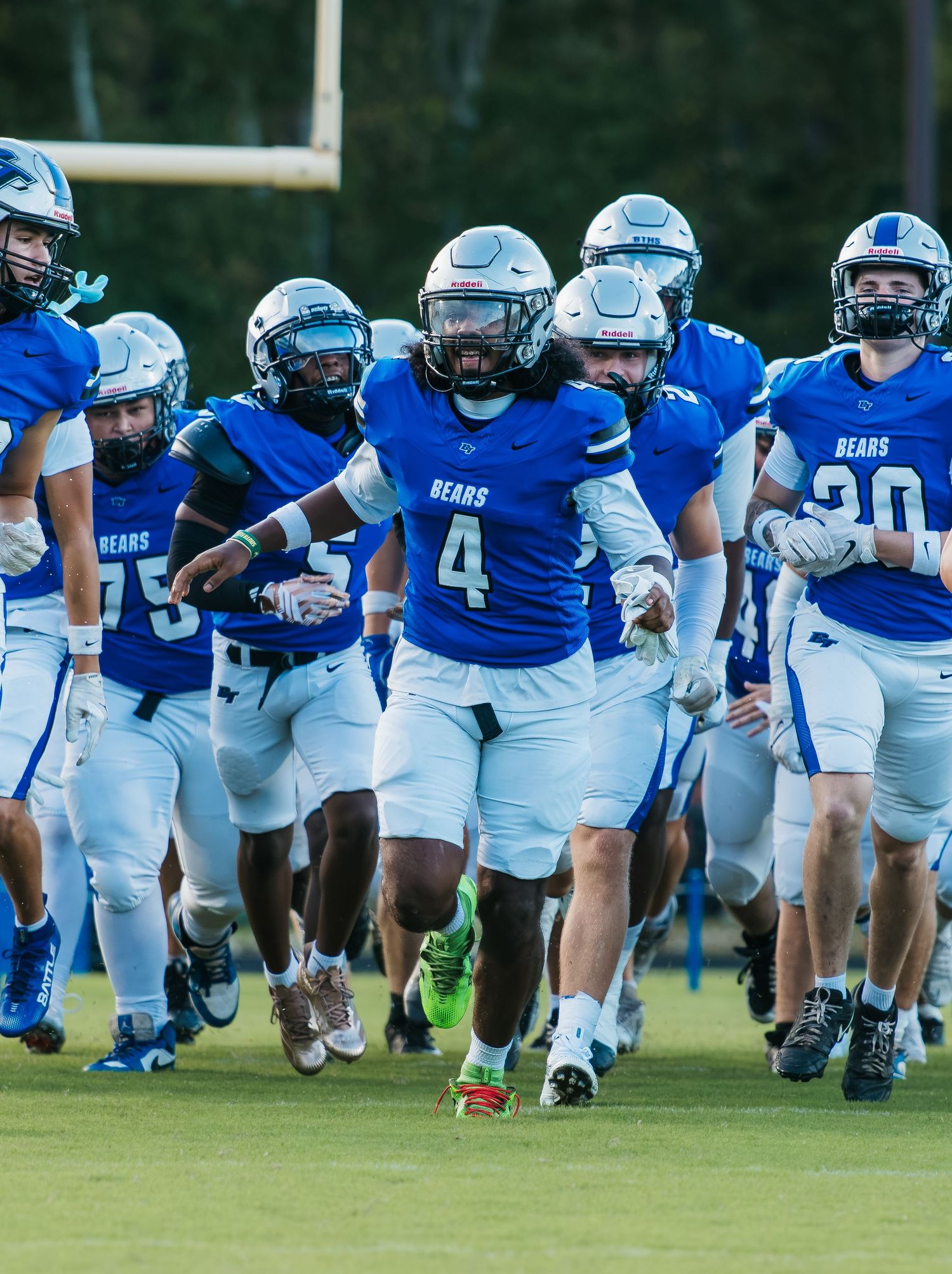 Blue Bears football team in uniform running onto field during a night game, led by player number 4.
