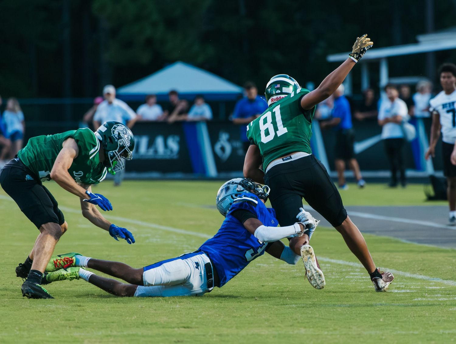 Football player #81 in green jersey evades tackle during competitive high school football game under stadium lights.