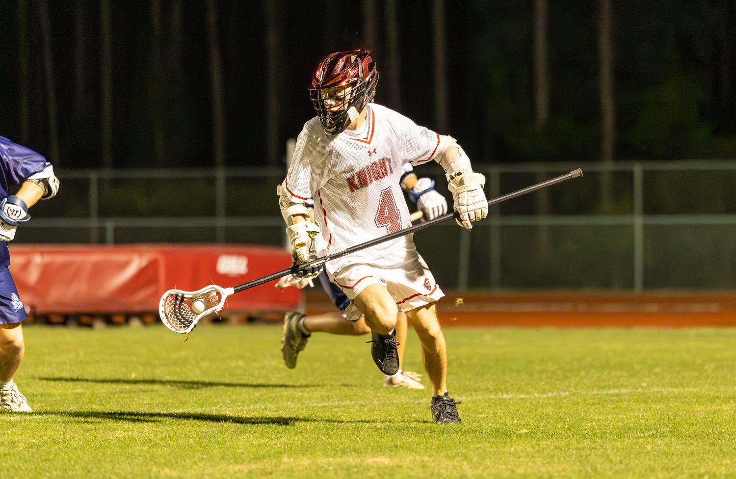 Lacrosse player in white jersey number 4 running with stick on field during night game.