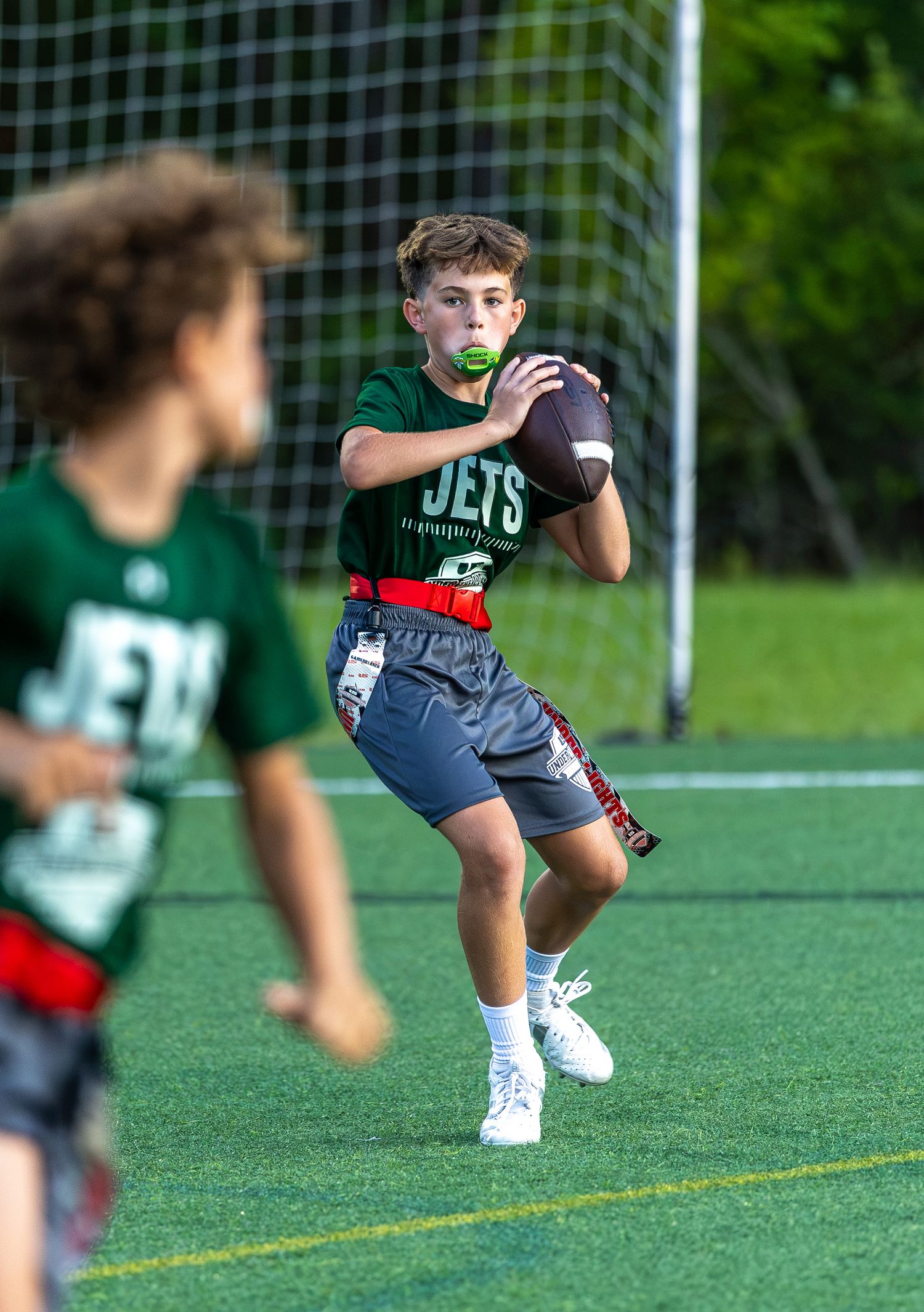 Young boy in Jets jersey catches football during flag football game on turf field.
