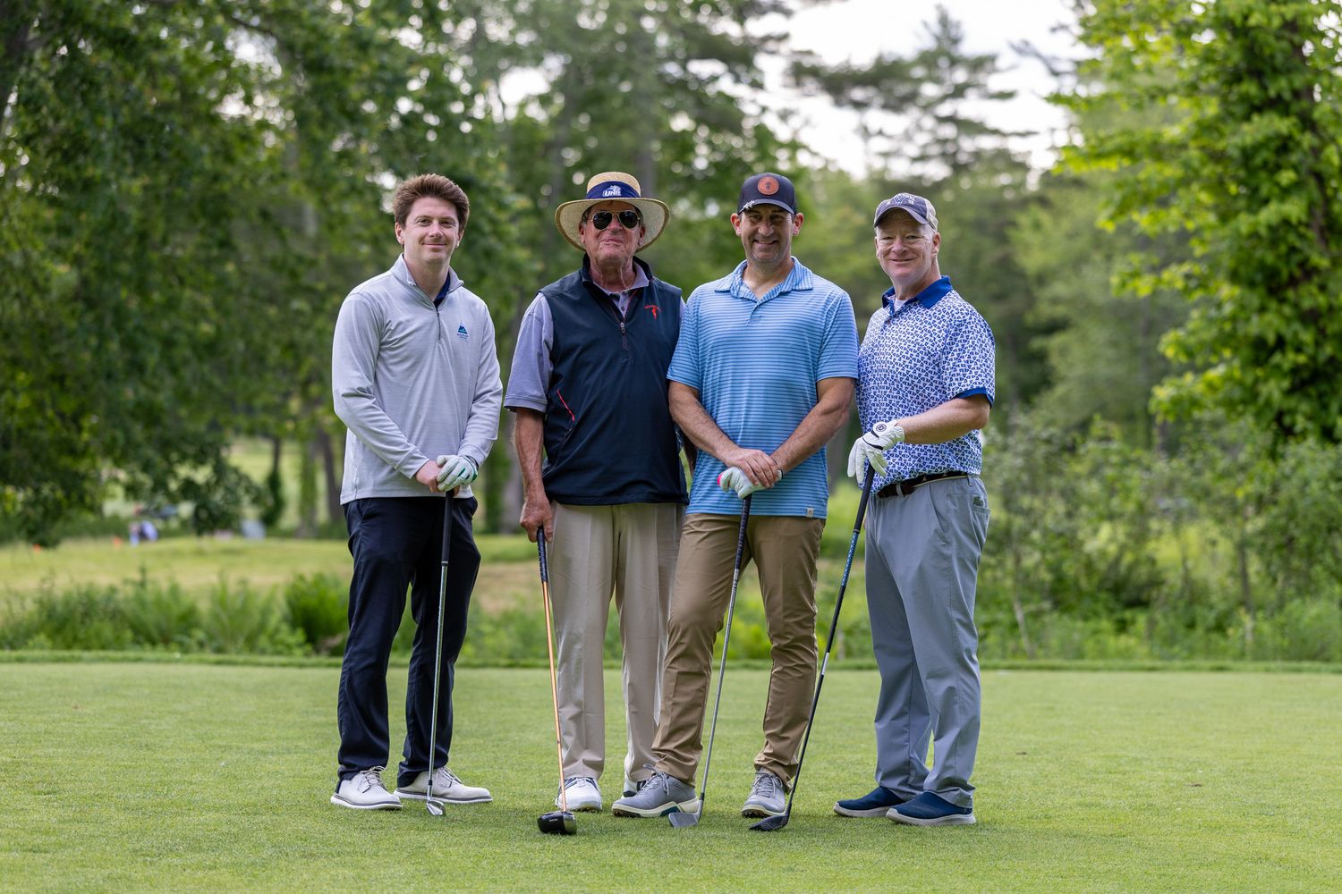 Four men posing together on a golf course surrounded by lush green trees during a golf outing.
