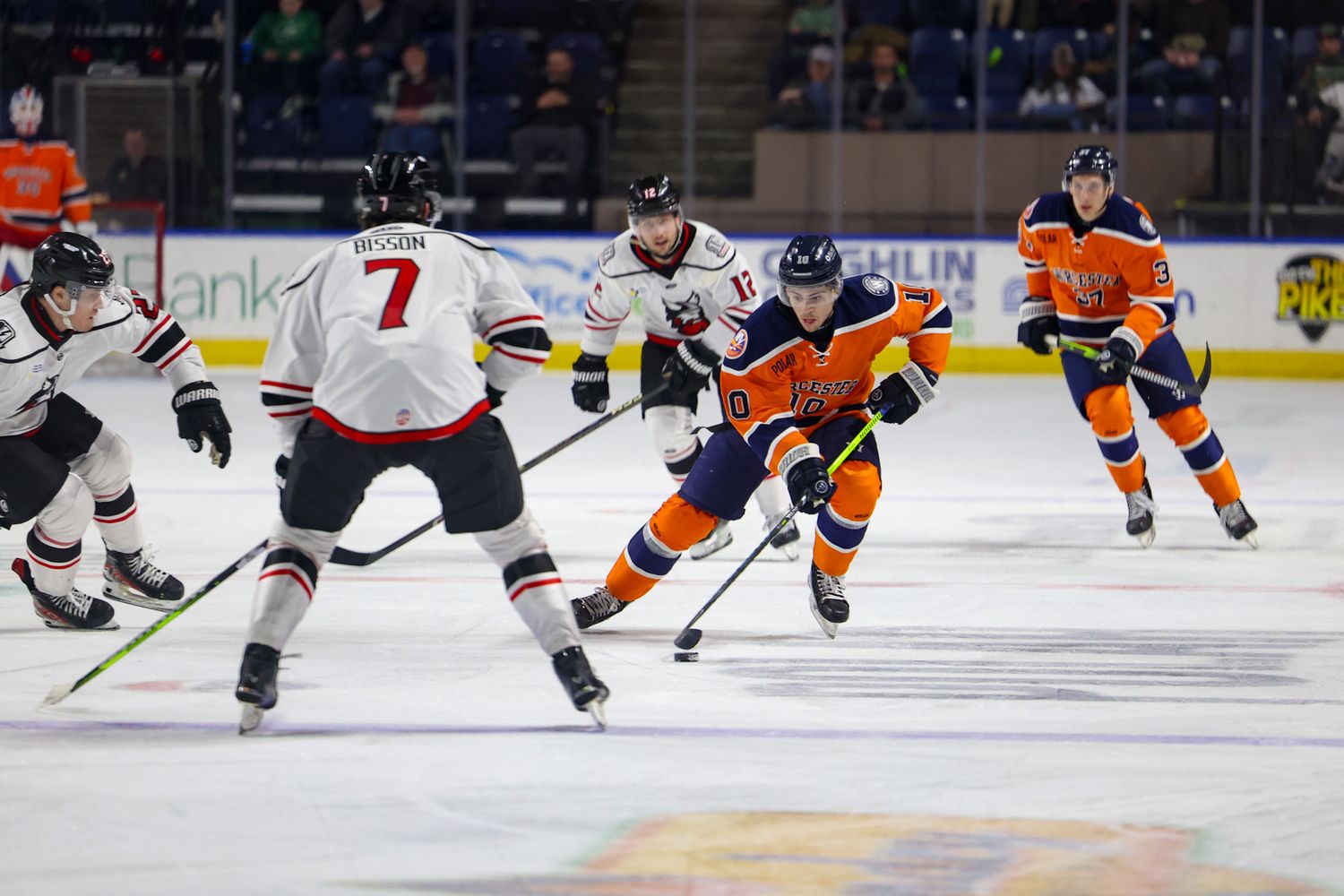 Ice hockey players in orange and white uniforms battle for the puck during a game.