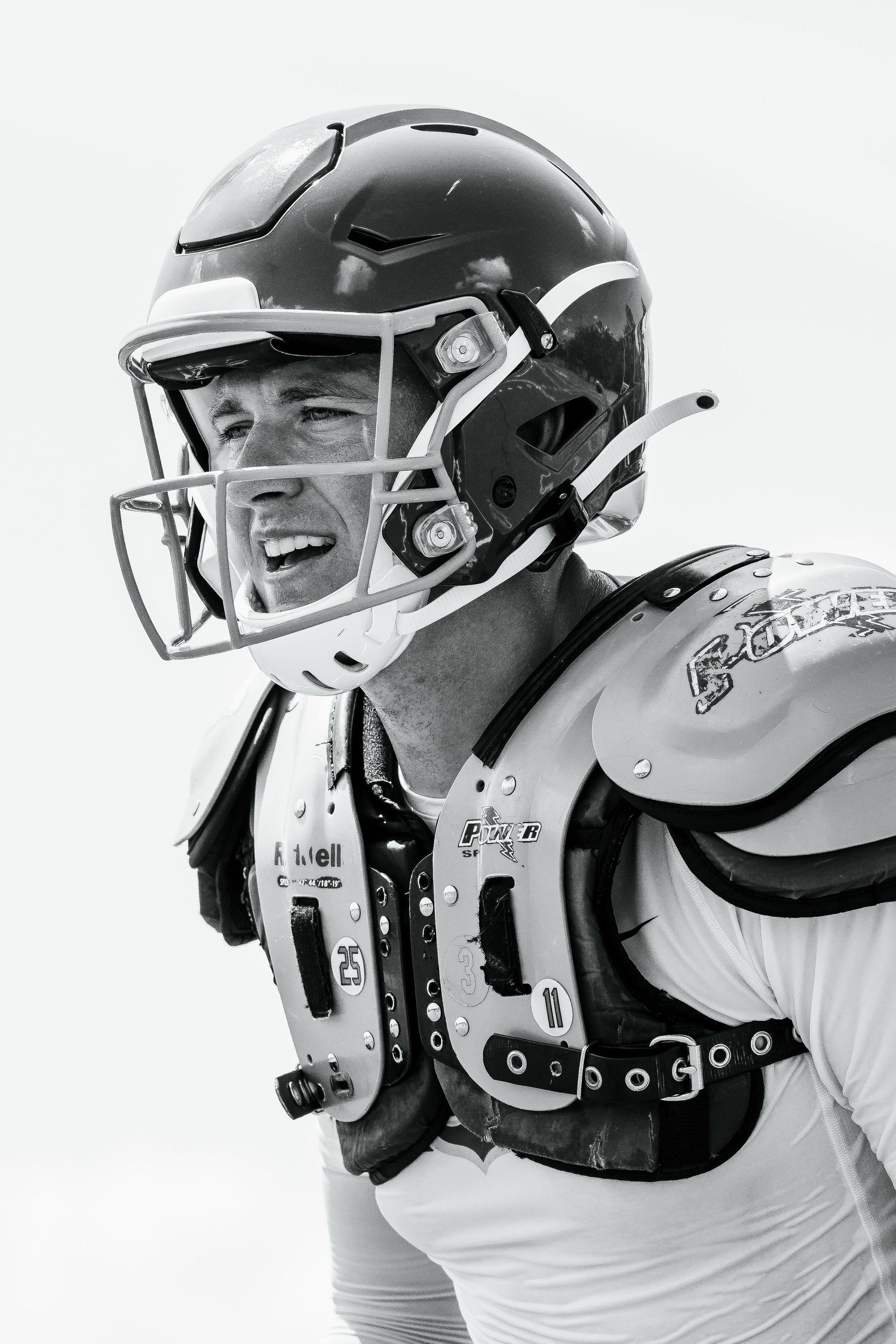 Black and white portrait of an American football player in helmet and shoulder pads, intense game-ready expression.