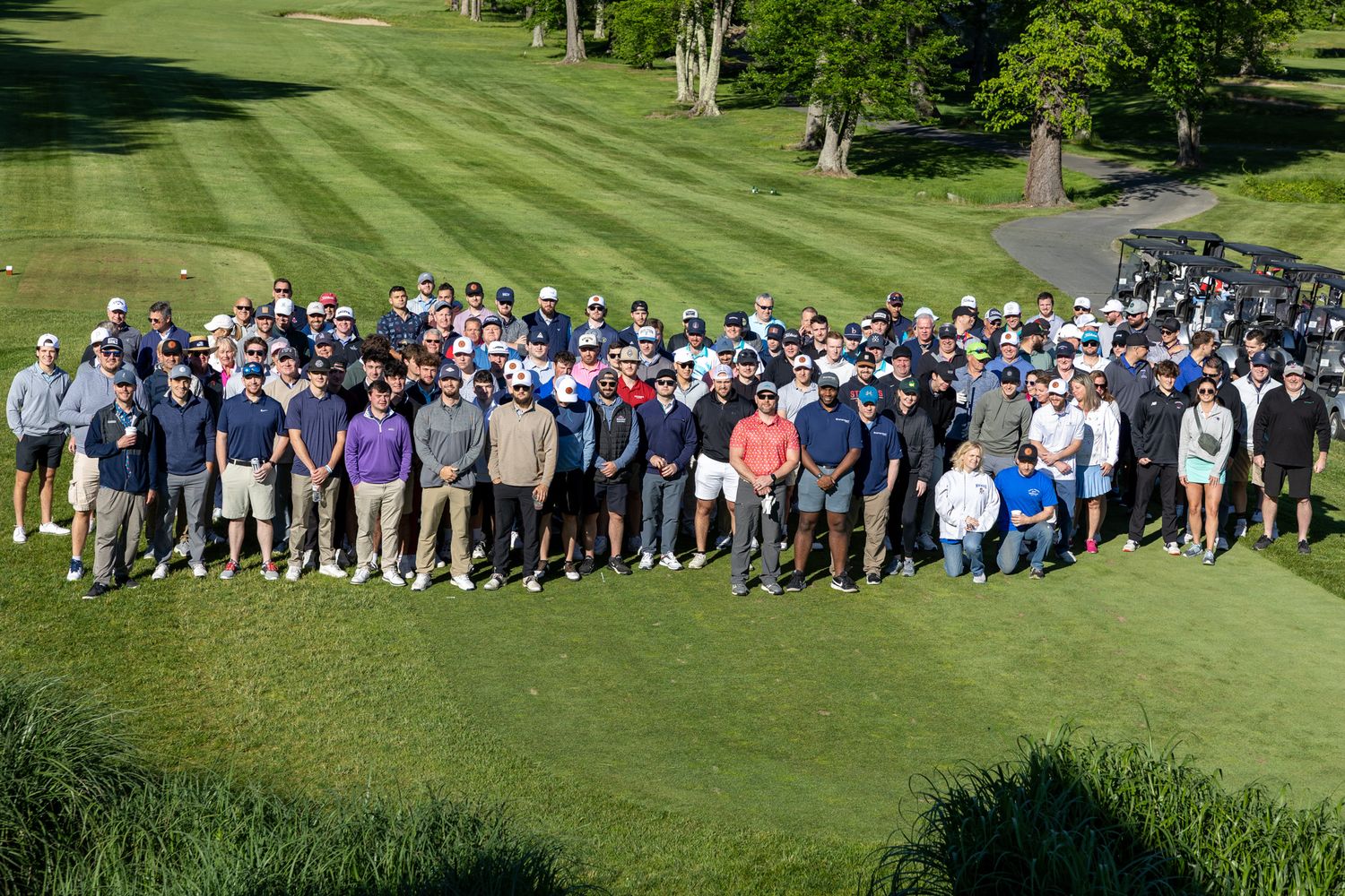 Large group of golfers posing together on a lush green golf course during a sunny outdoor tournament event.