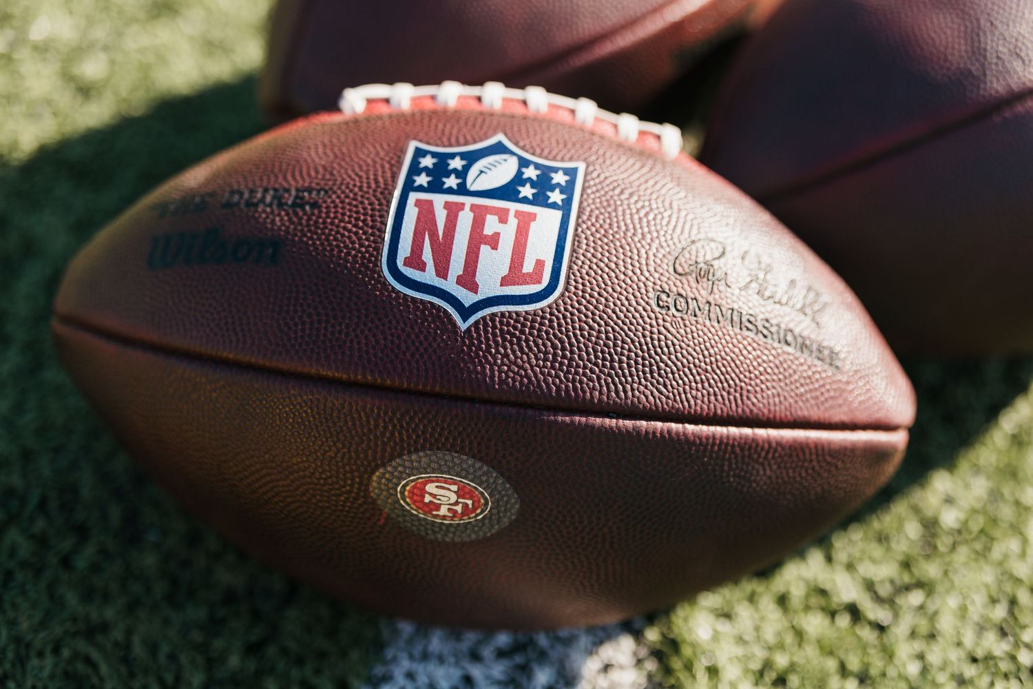 Close-up of an official NFL Wilson football with San Francisco 49ers logo on green grass field.