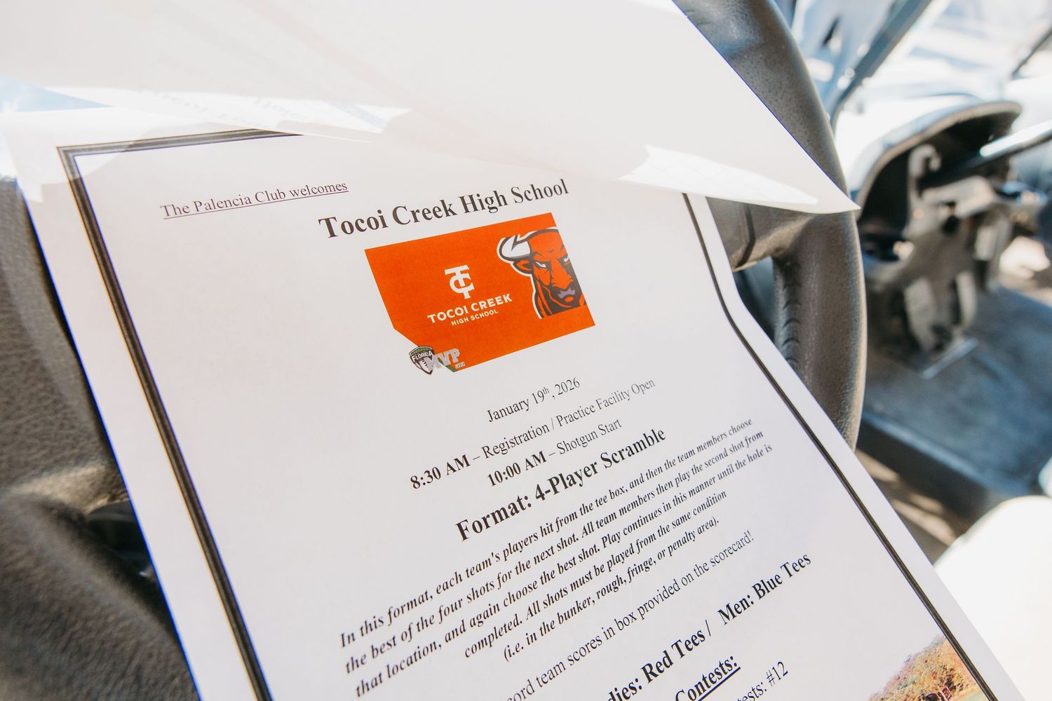 Tocoi Creek High School golf scramble event flyer resting on a car seat with tournament details visible.