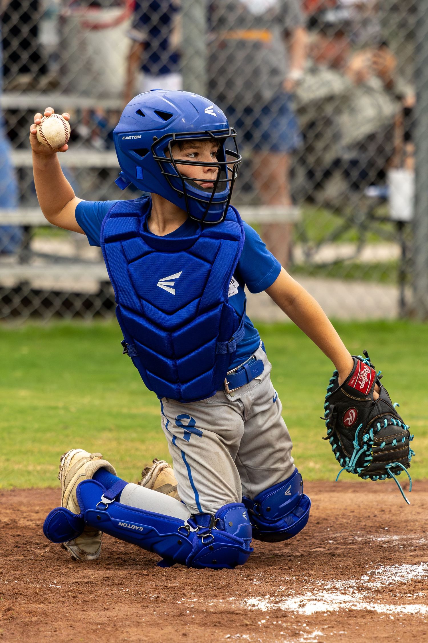 Young baseball catcher in blue Easton gear throws ball during little league game.