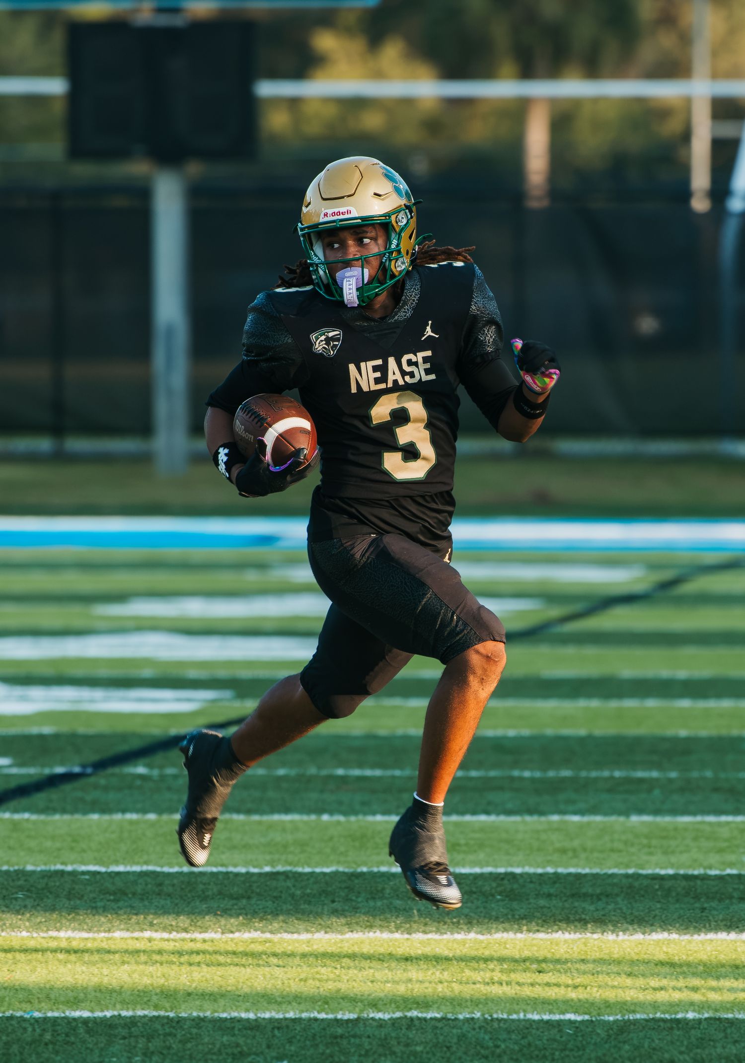 Nease High School football player #3 in black uniform runs with the ball on a green turf field.