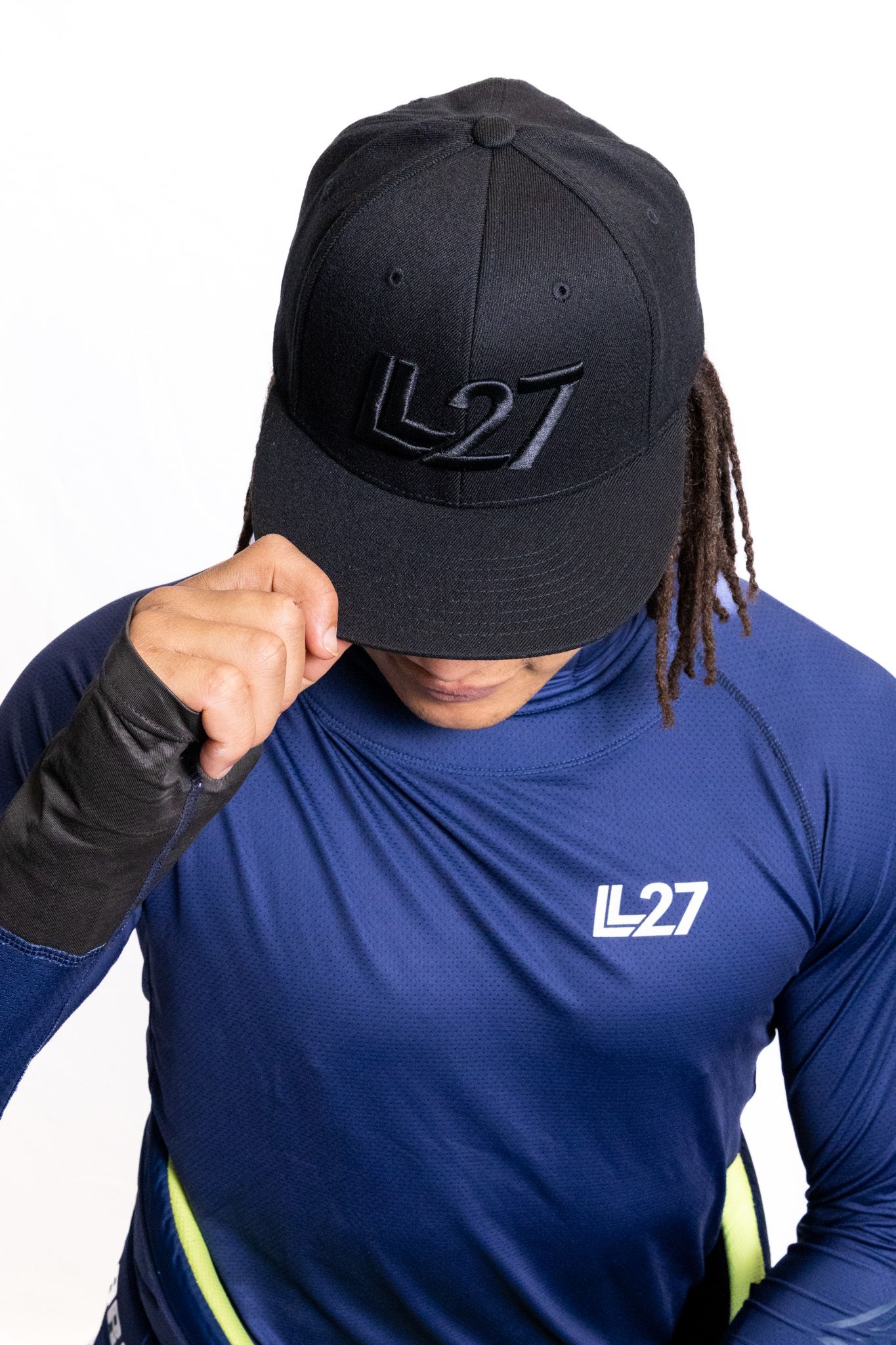 Person wearing a black LL27 snapback cap and navy blue LL27 long sleeve athletic shirt, posing with cap tilted down.