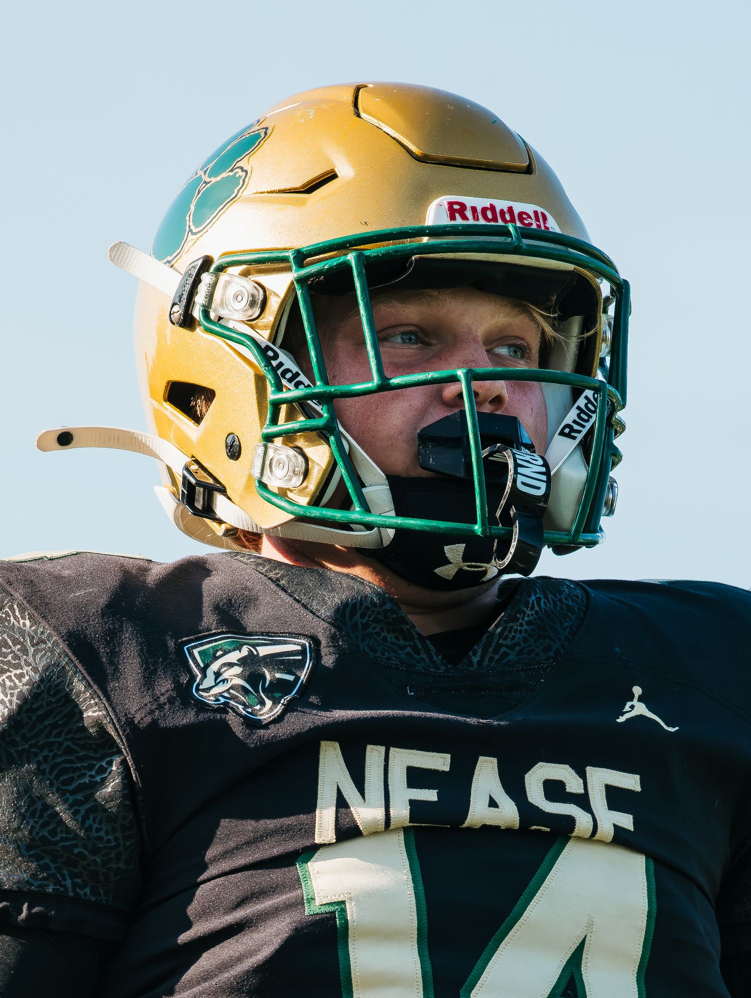 Nease high school football player wearing gold Riddell helmet and dark jersey with number 14 on the field.