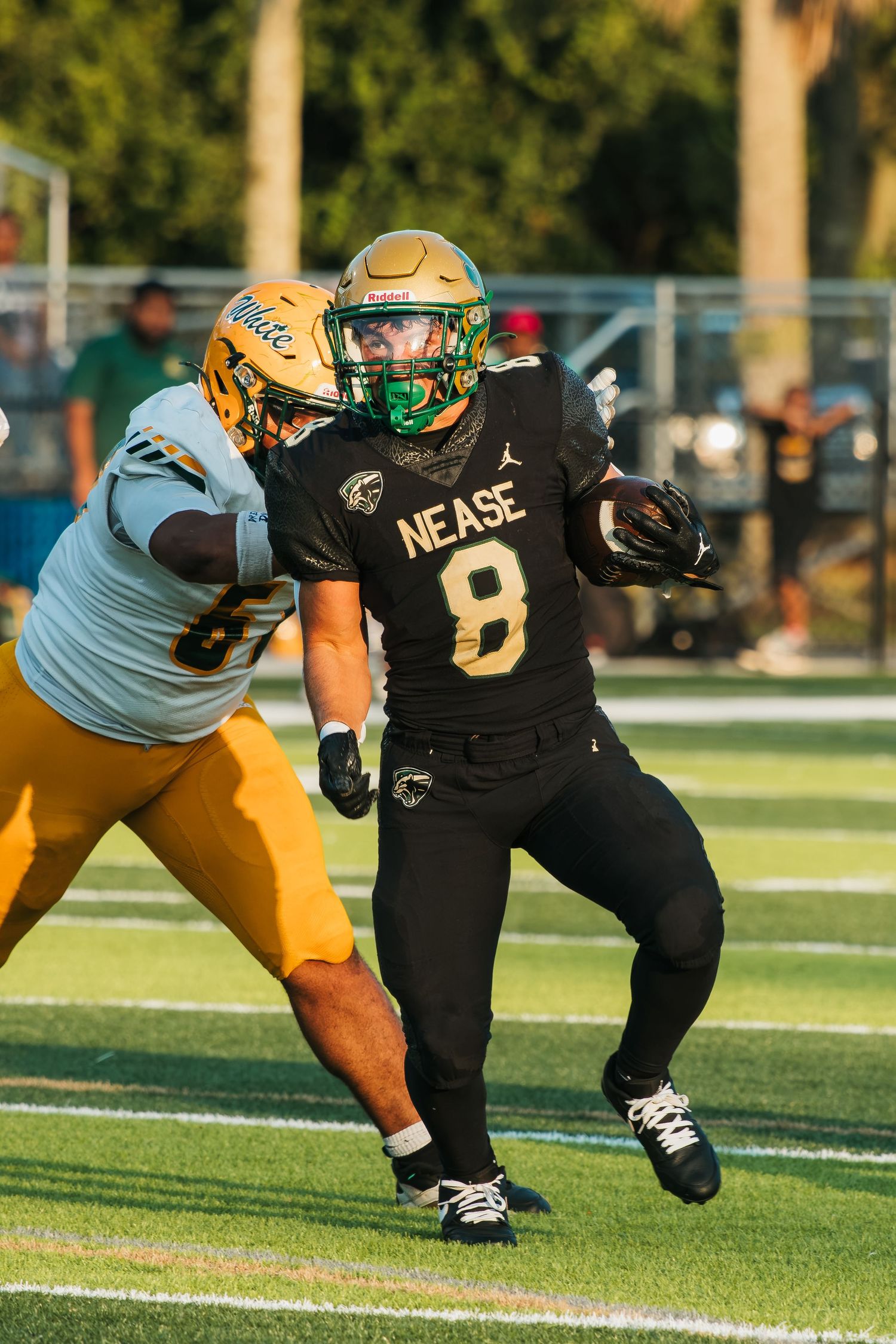 Nease #8 football player in black uniform runs with ball while opponent in yellow jersey attempts tackle.