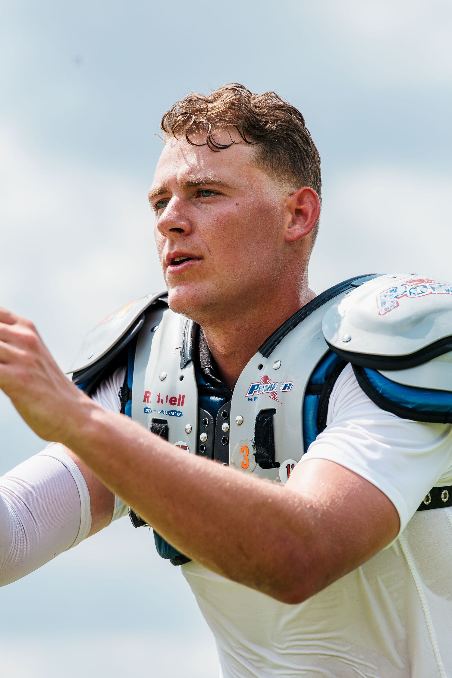 Football player in white uniform and Riddell shoulder pads gestures on the field during a sunny outdoor game.